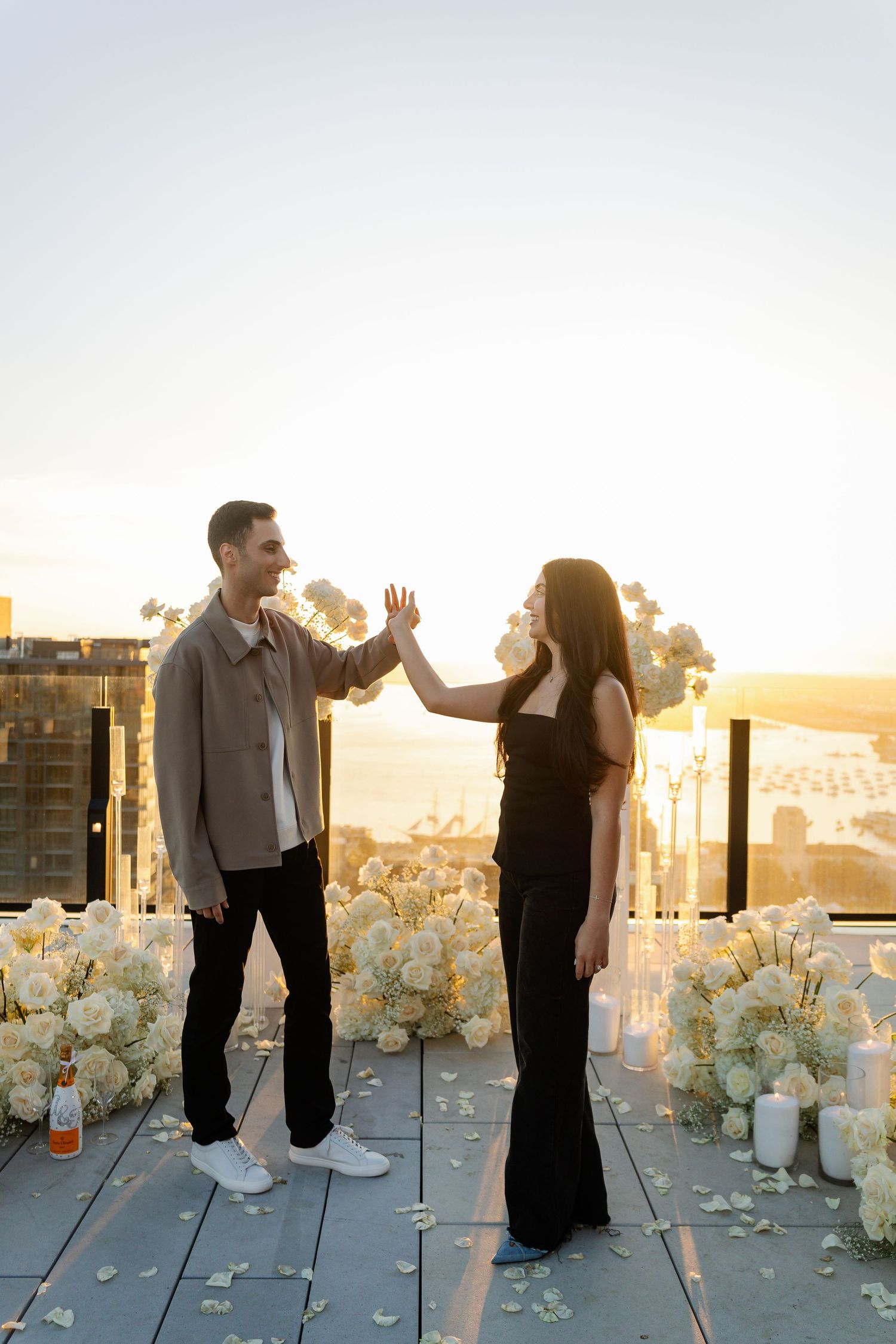 A couple shares a playful moment among white floral decorations on a rooftop.