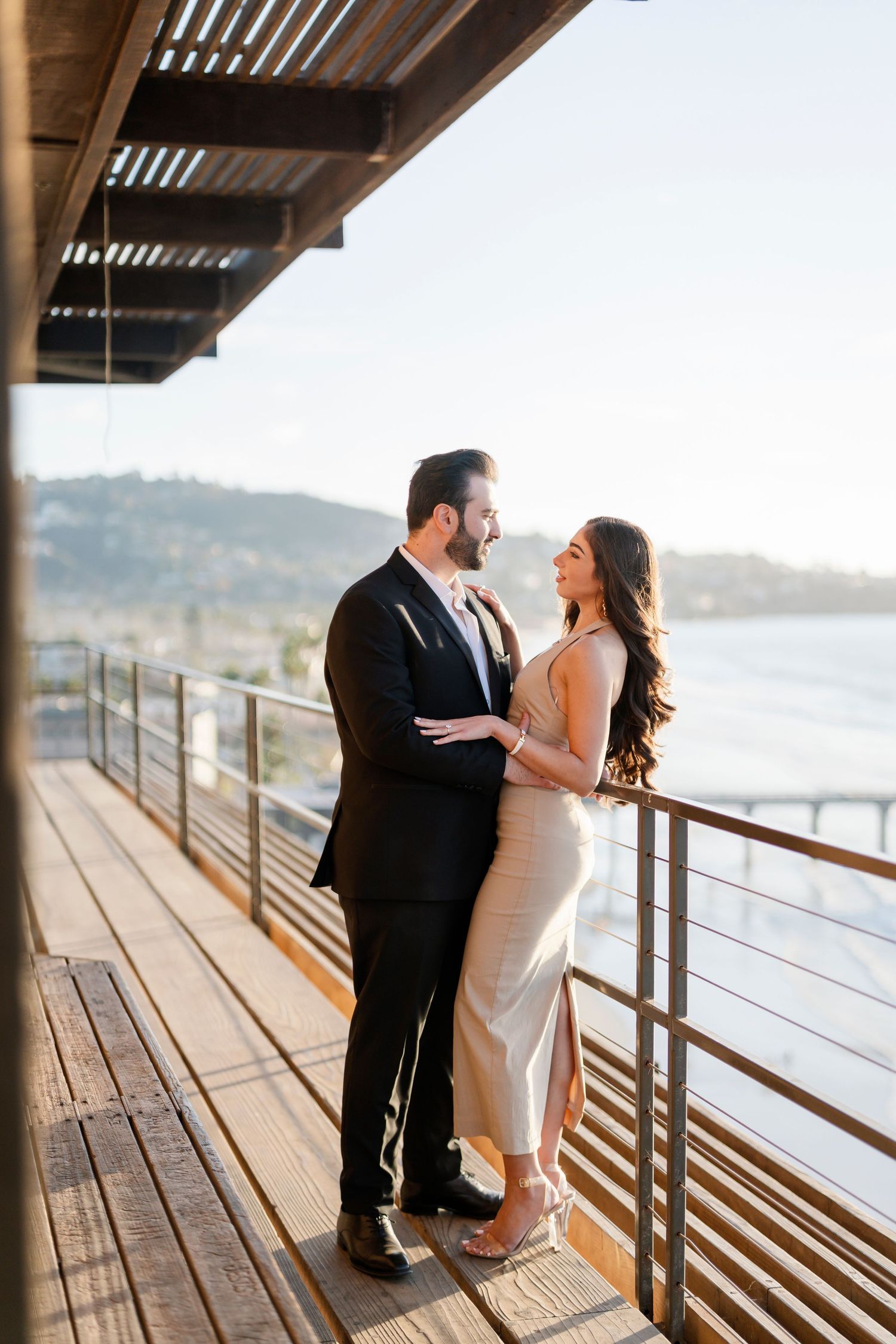 Couple shares intimate moment on wooden deck overlooking coastal waters.