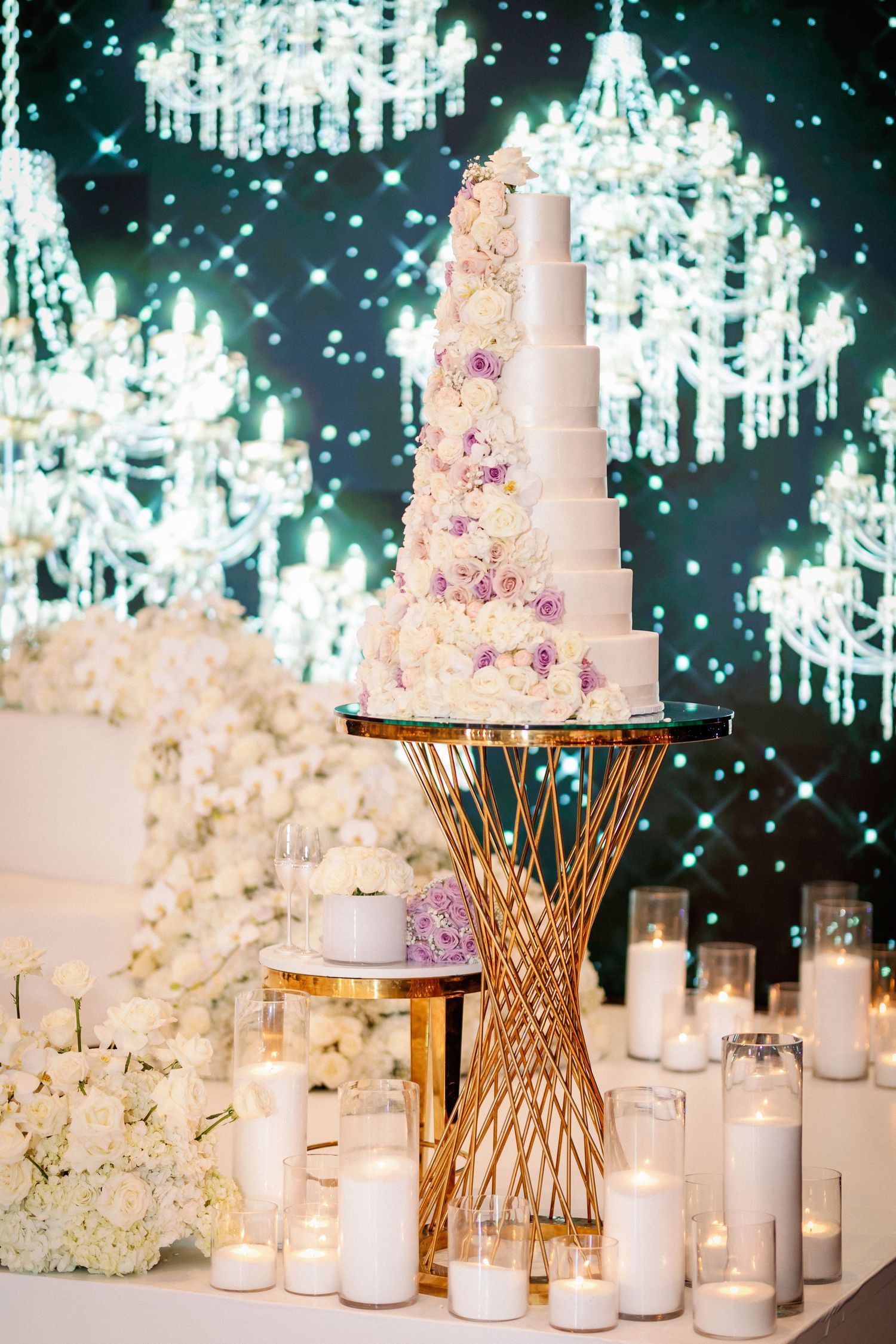 Elegant wedding reception decor with white floral arrangements, crystal chandeliers, and glowing candles on gold stands.