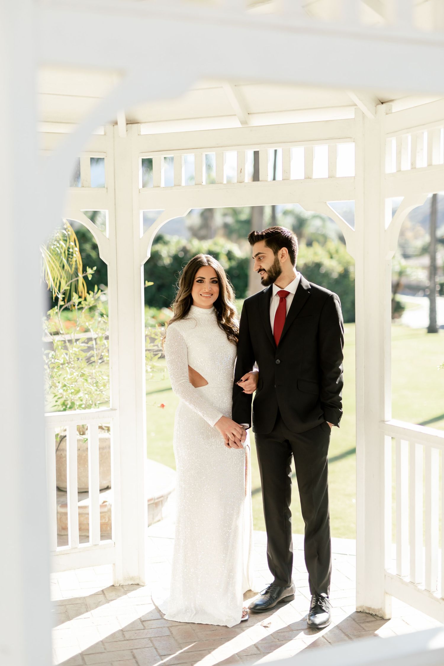Couple poses in white gazebo for wedding photos in natural lighting.