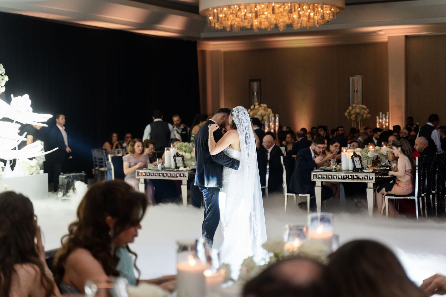 Wedding reception venue with elegant lighting and guests dancing on a white dance floor.