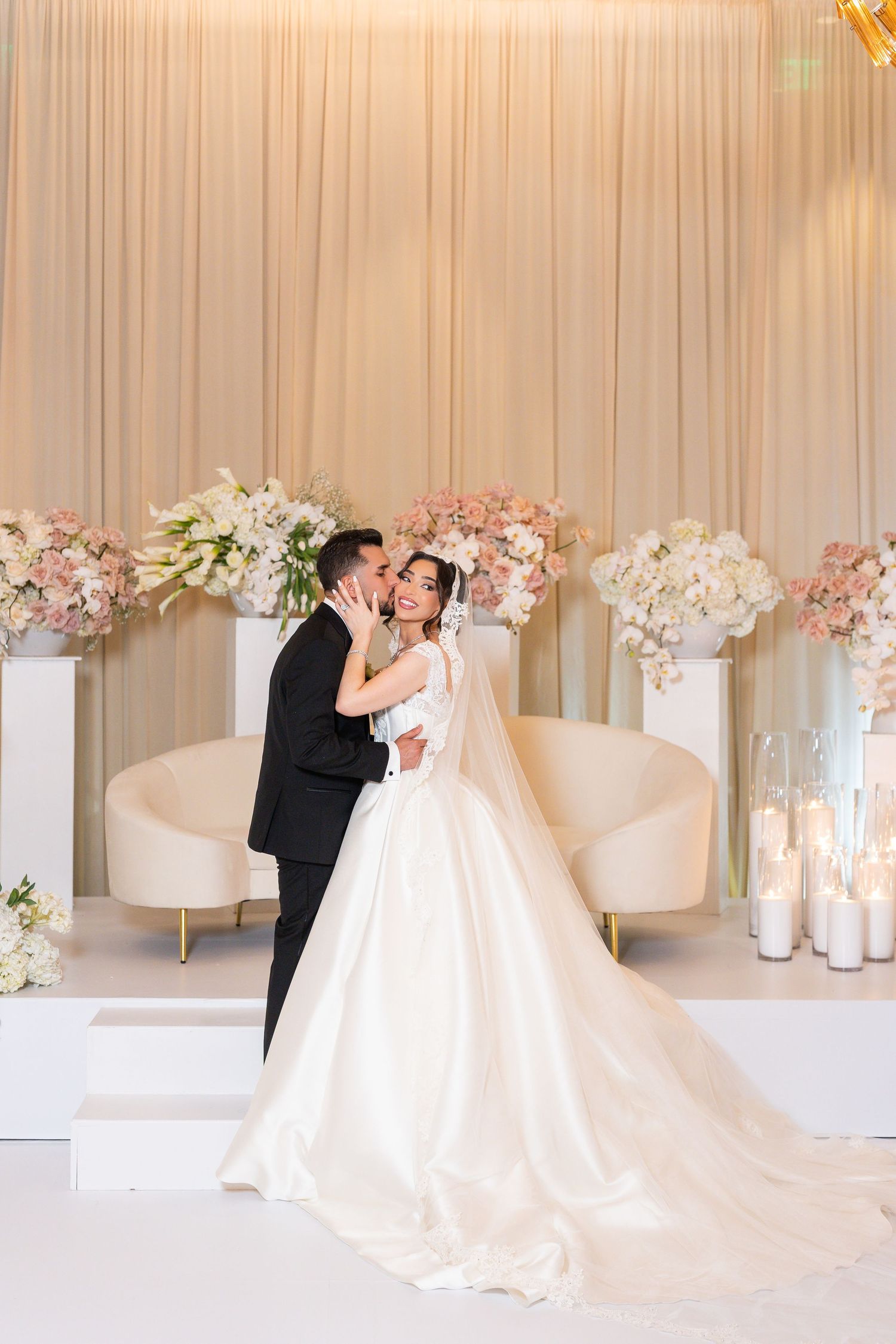 Wedding celebration in an all-white venue decorated with pink floral arrangements and flowing drapery.