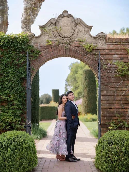 A romantic moment captured under an ornate brick archway in a formal garden.