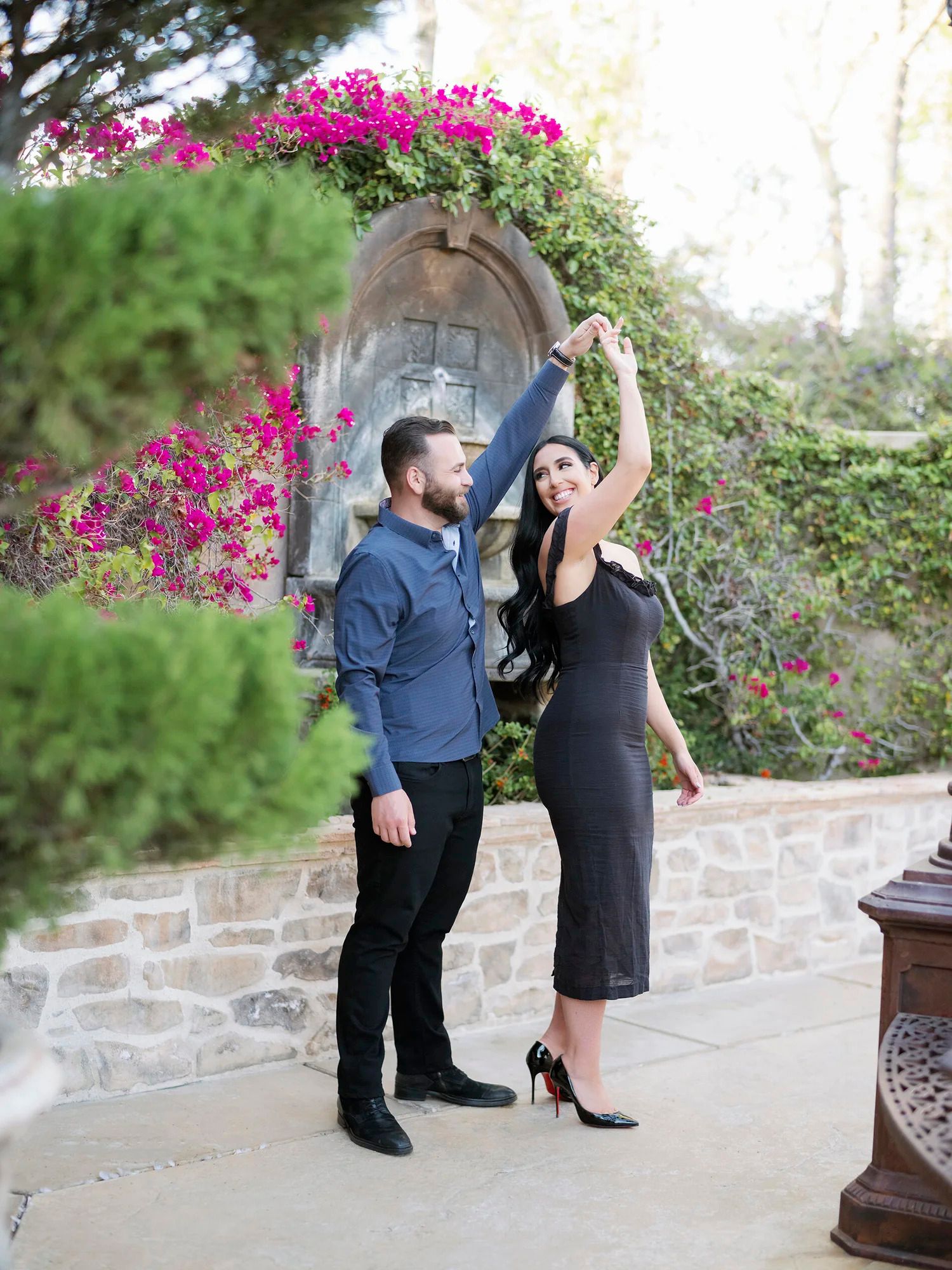 A couple dances together on a stone patio surrounded by vibrant pink bougainvillea.