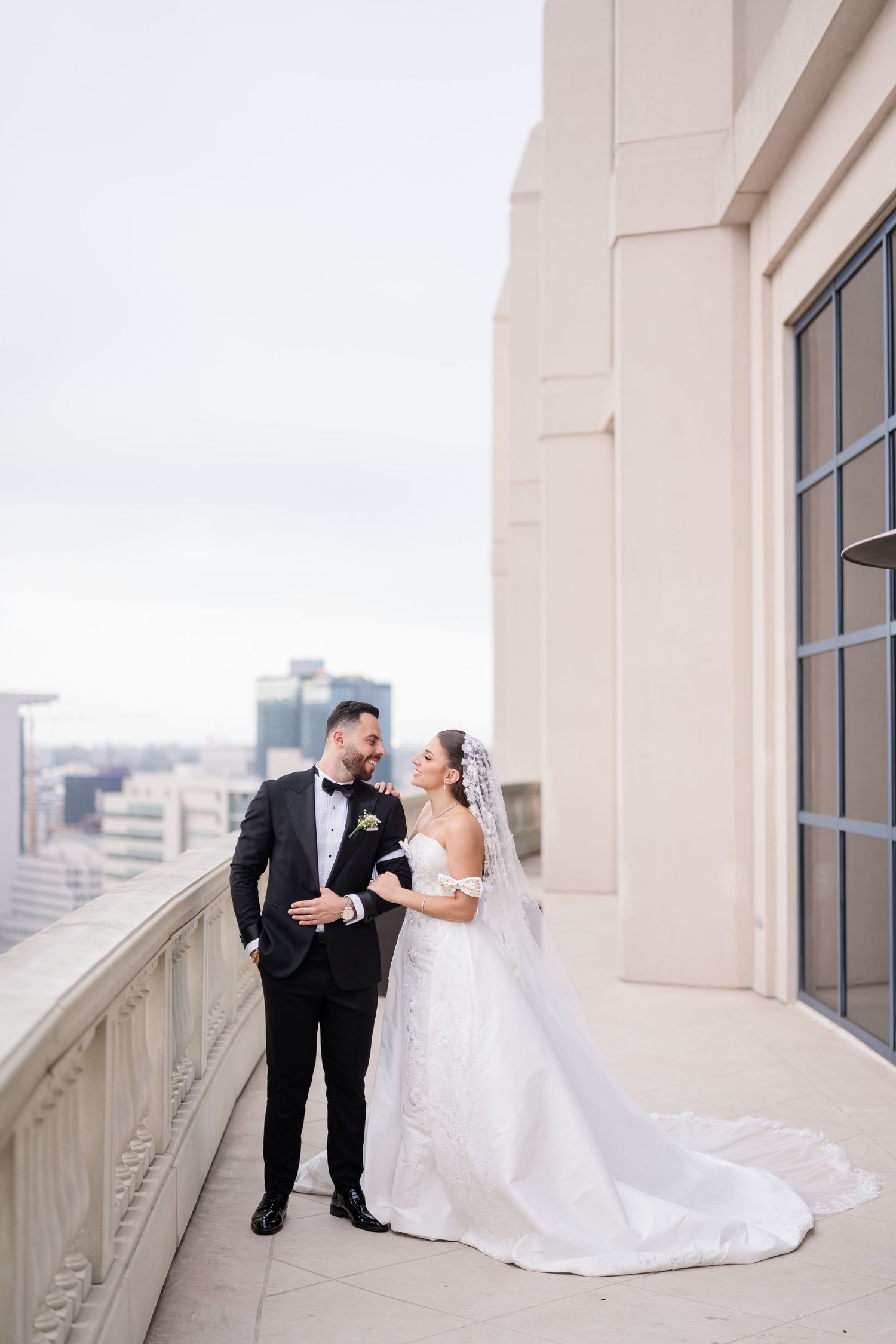 Romantic wedding photos taken on an elegant outdoor balcony with city views.