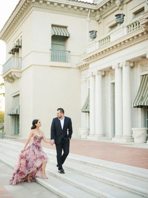 Couple in formal wear poses on grand white stone steps of classical building.
