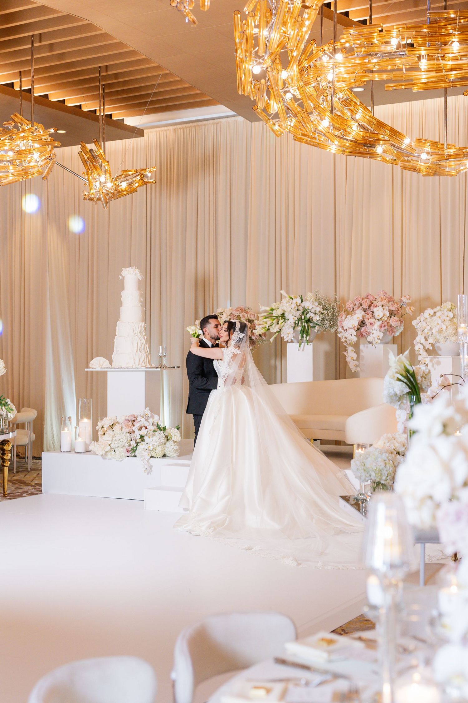 Luxurious wedding reception space featuring golden lighting fixtures and white draped walls.