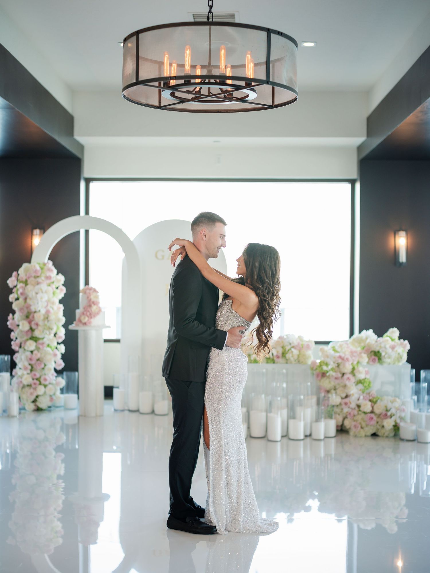 Elegant couple dances in a bright modern venue decorated with white floral arrangements.
