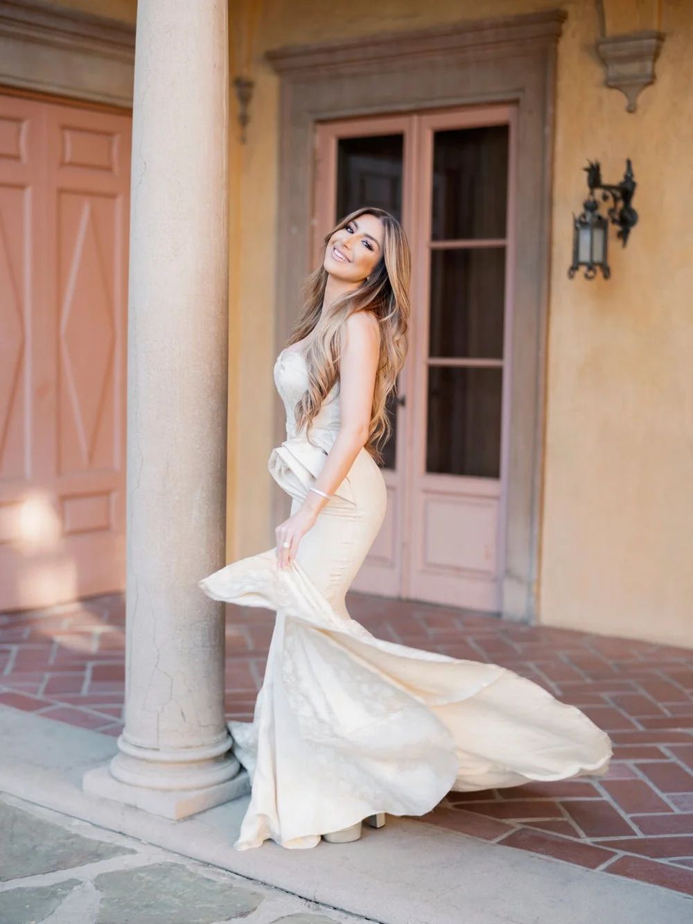 Elegant white dress flowing against peach-colored colonnade with terracotta tile flooring.