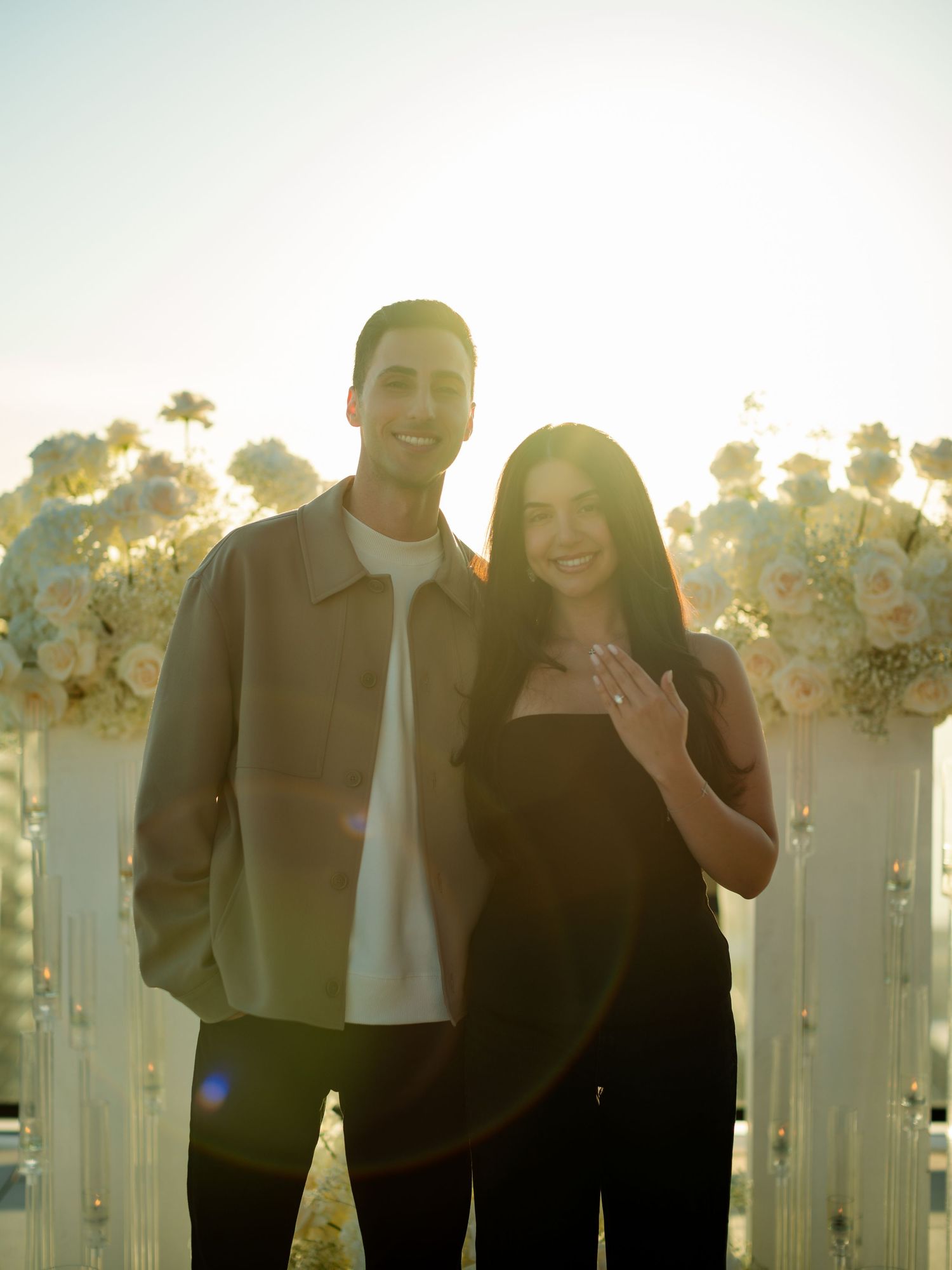 A couple shares a joyful moment surrounded by white floral decorations at sunset.