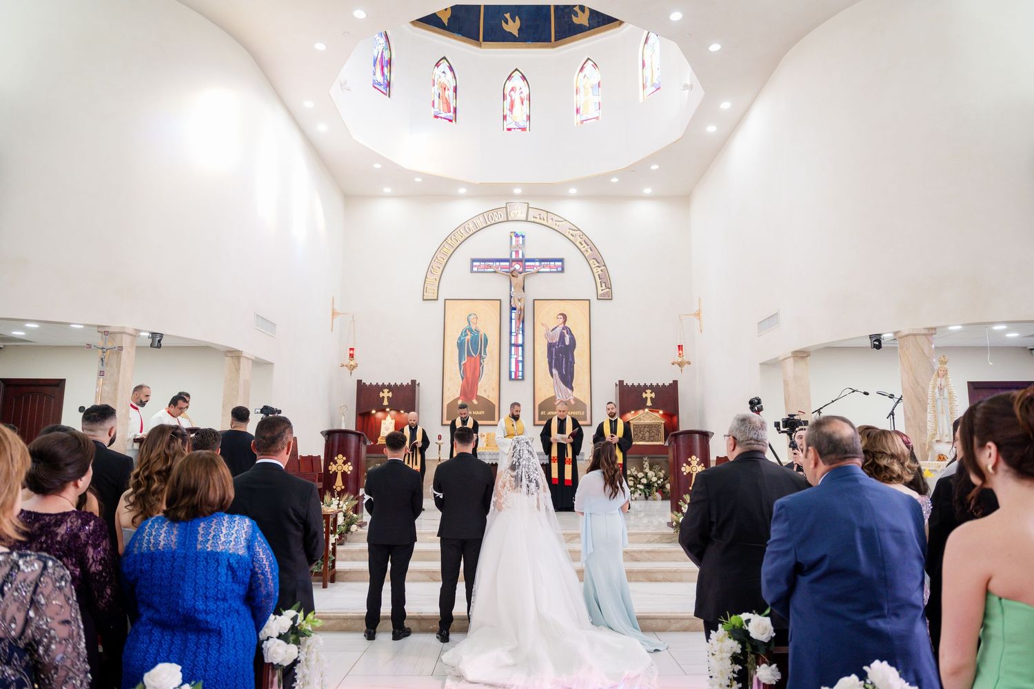 Panoramic view of a church wedding ceremony with guests seated in white pews.