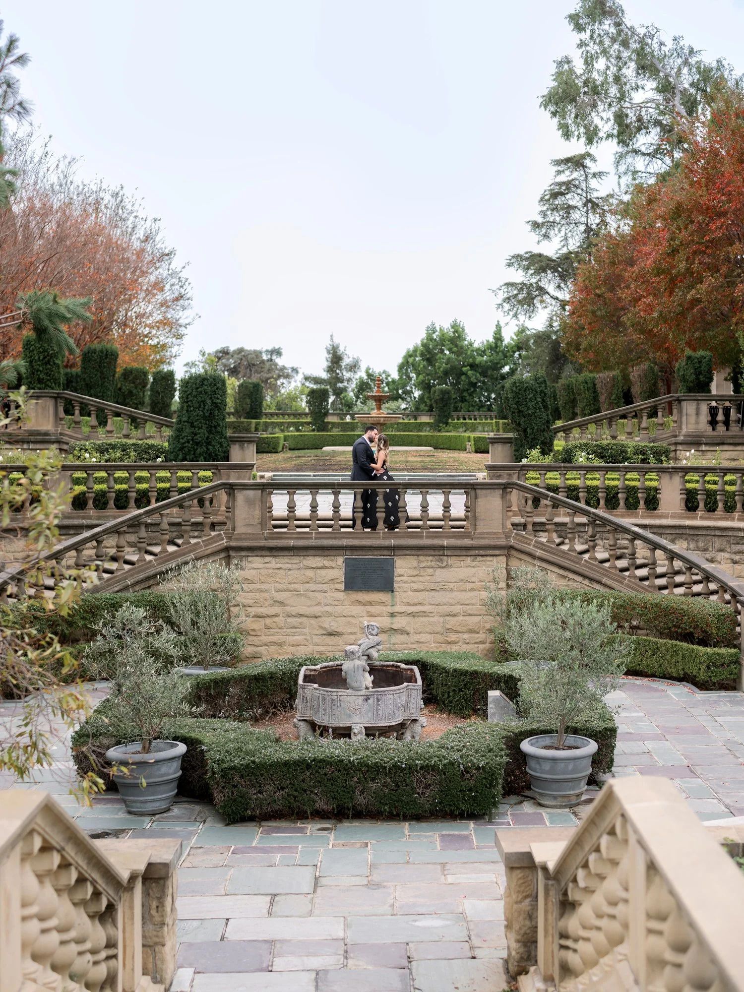 A formal garden terrace with symmetrical steps, hedges and a central fountain.