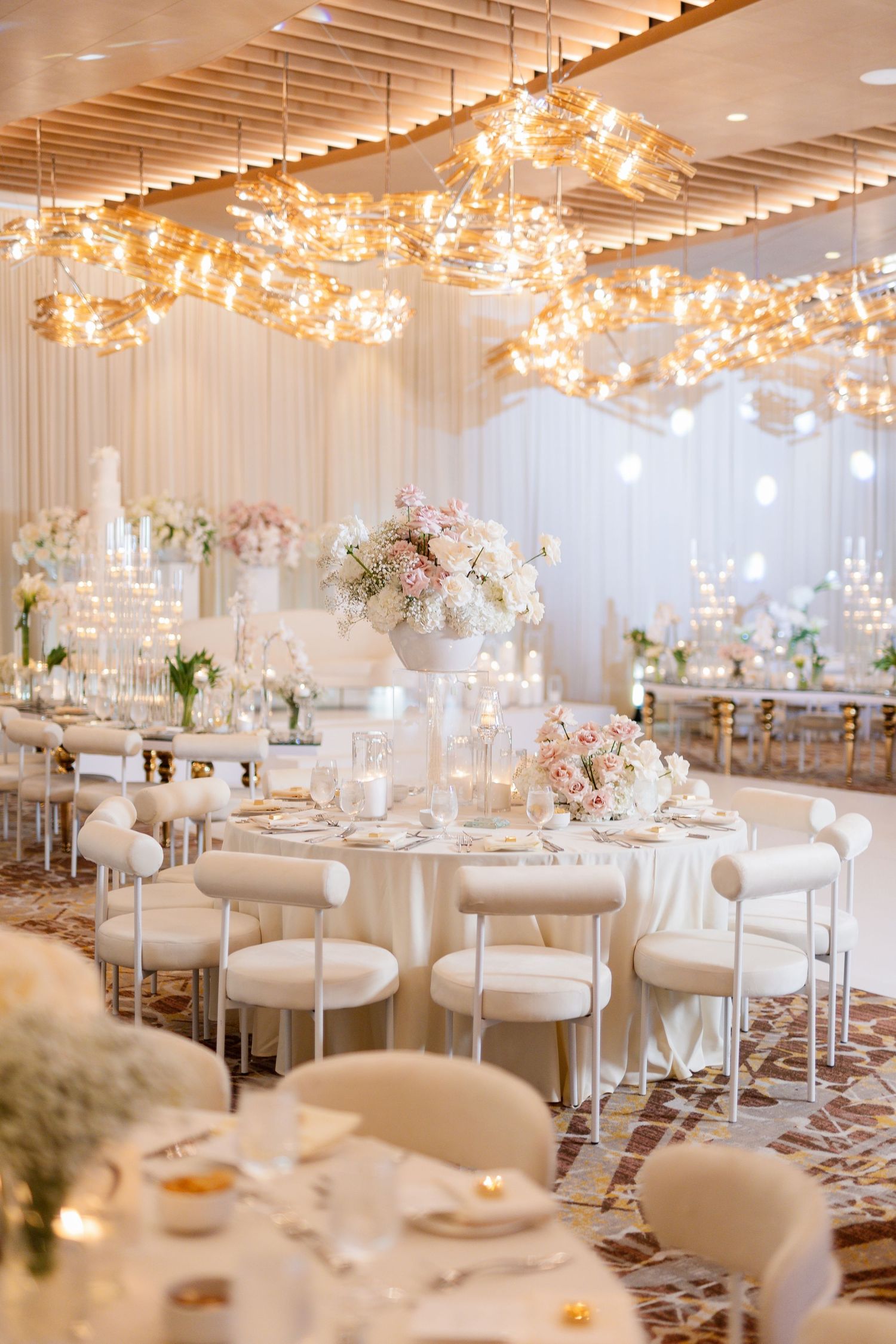 Modern wedding reception hall with white furniture and dramatic overhead lighting.