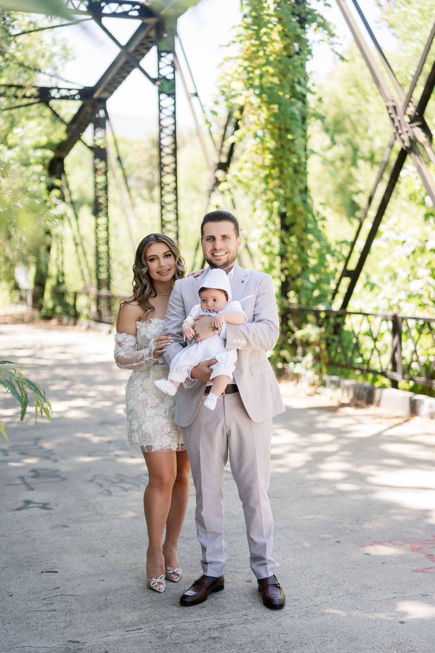 A mother and child in matching white outfits dance together in a sunlit garden path with ivy-covered structures.