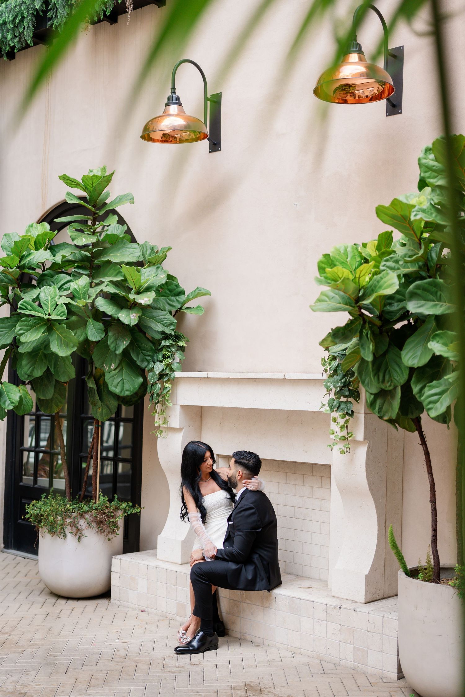 An intimate photoshoot in an elegant courtyard with fiddle leaf fig plants and copper lighting.