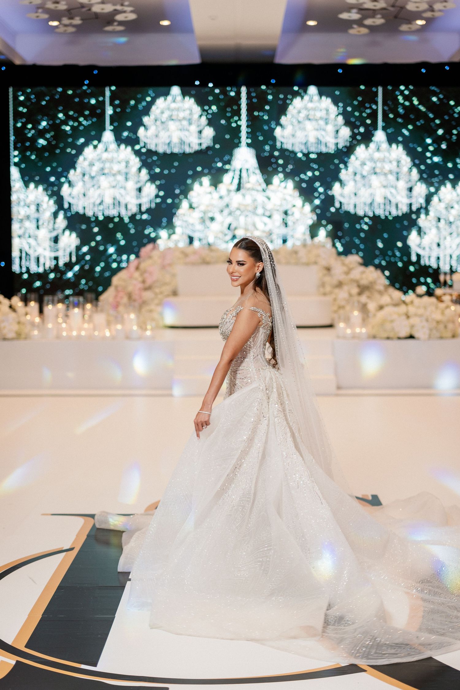 A stunning bridal gown with a flowing train displayed under elegant crystal chandeliers at a wedding venue.