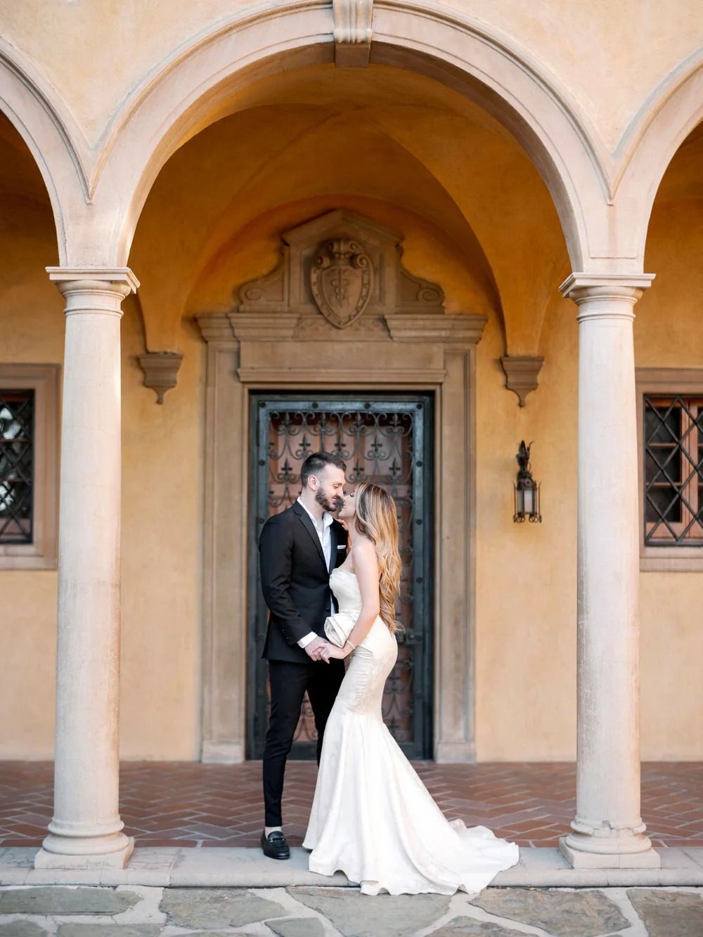 Romantic moment under arched colonnade with classical architectural details and warm lighting.