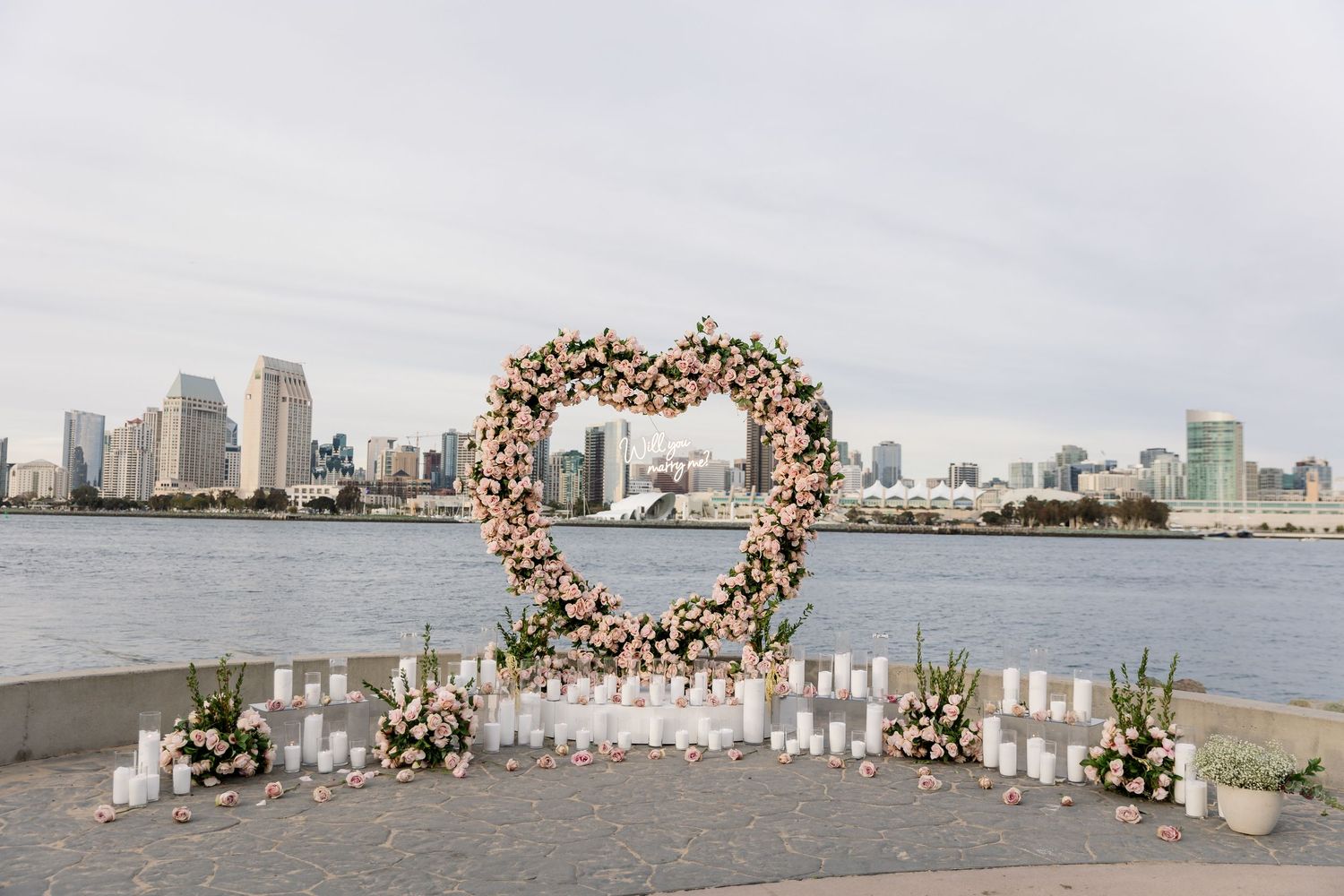 Heart-shaped floral installation with white candles set against an urban waterfront backdrop.