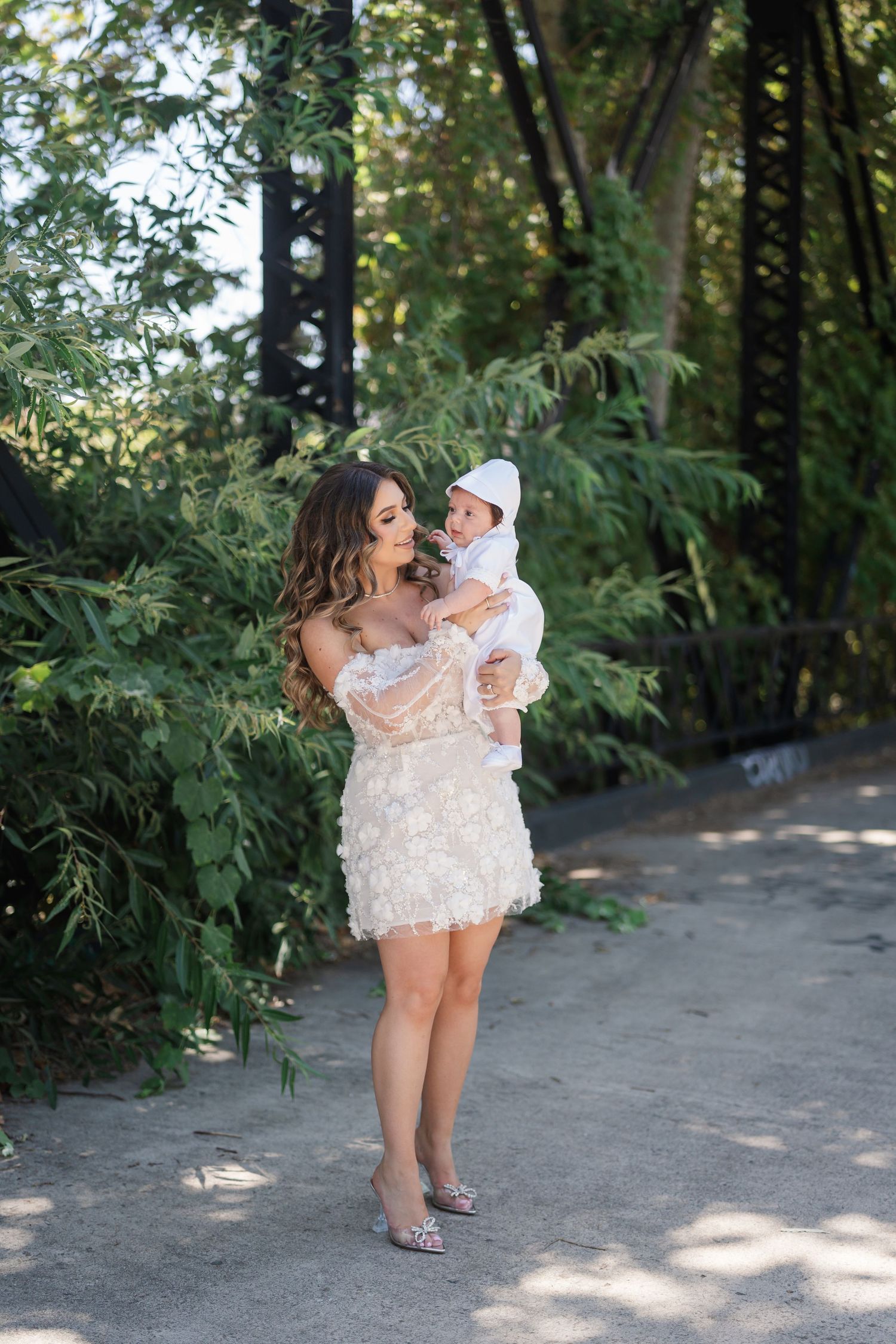 A tender moment between parent and child on a sunlit wooded path wearing matching white lace outfits.