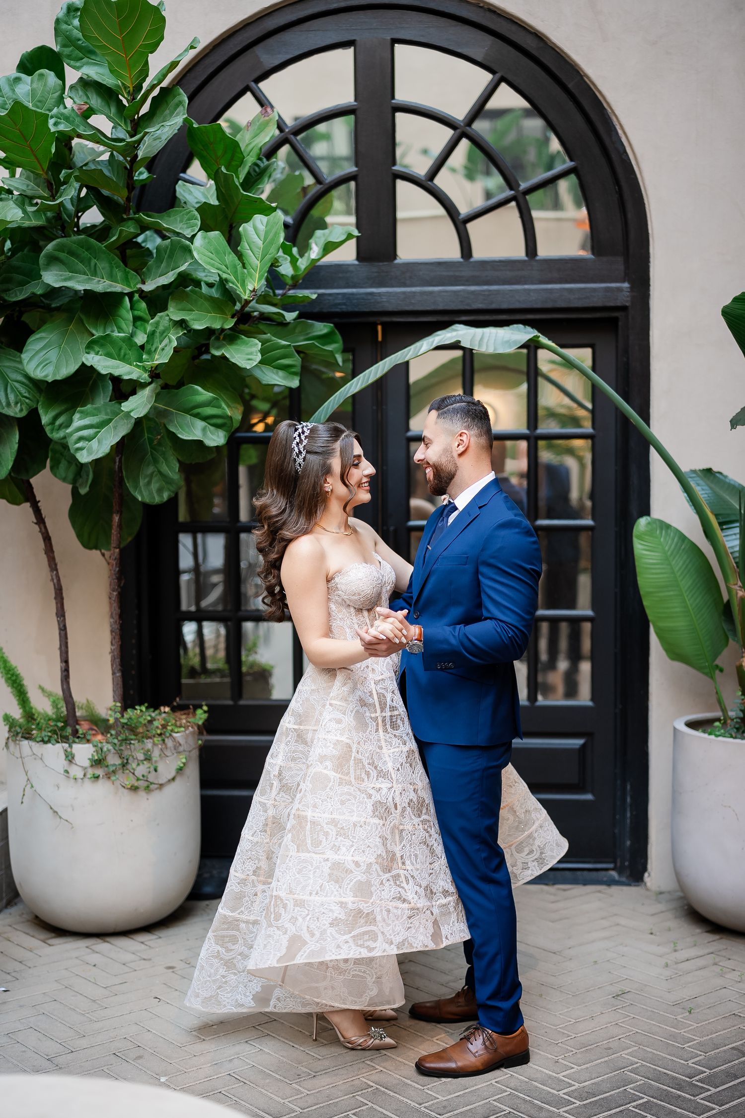Couple dances near black arched doorway with tropical plants in modern setting.