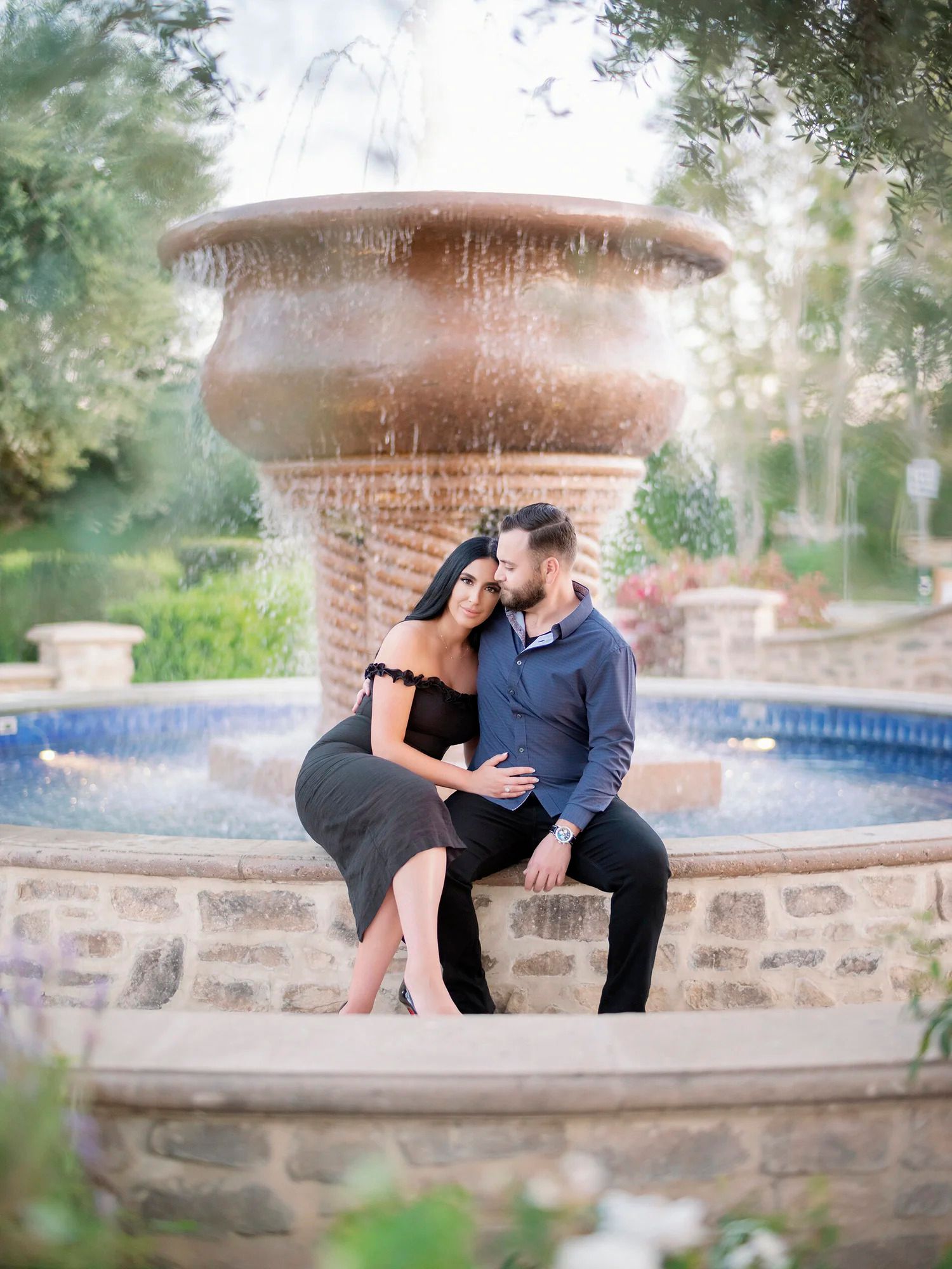 Couple sitting together on a stone fountain ledge in a romantic garden setting.