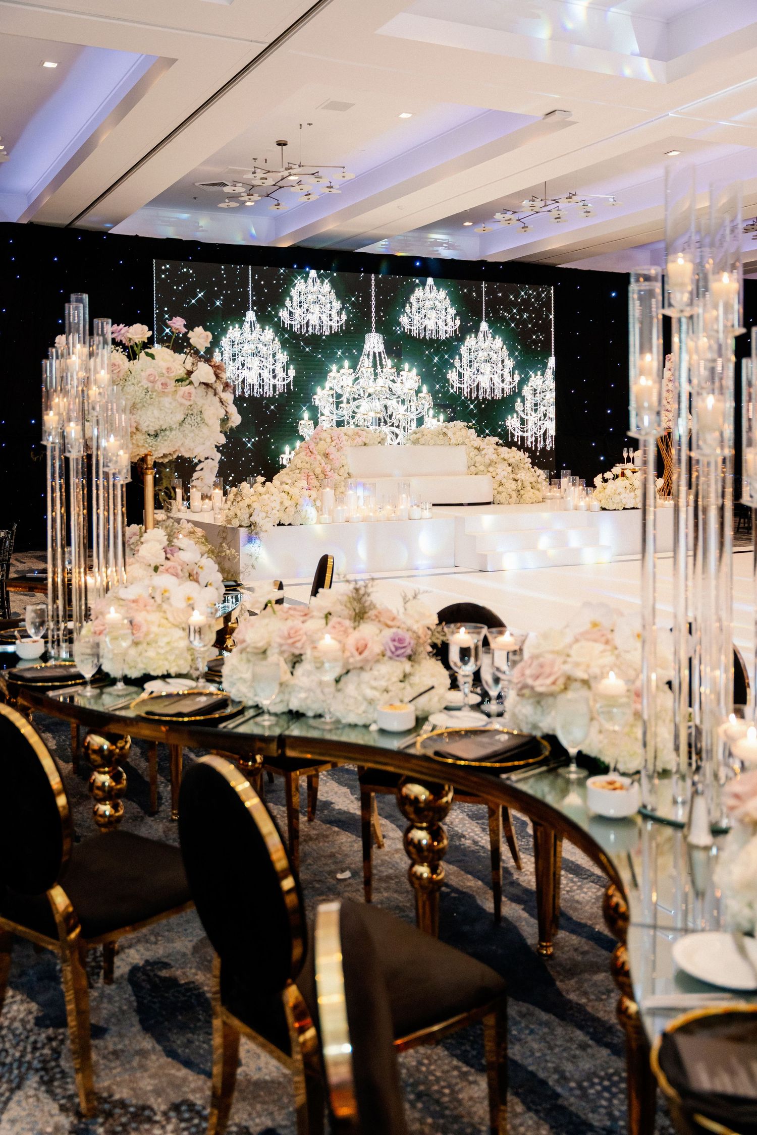 Elegant reception tables with crystal chandeliers and white floral centerpieces.