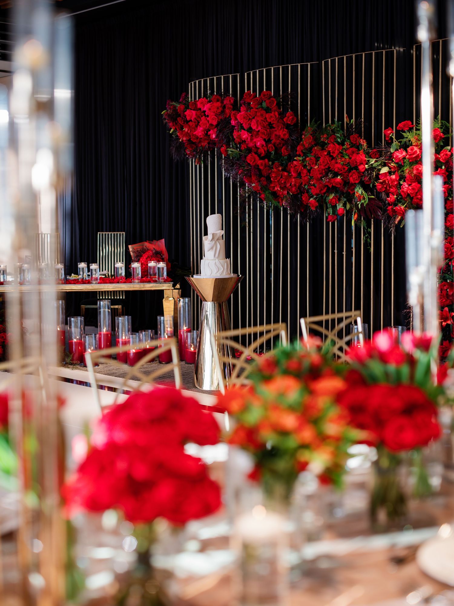 Luxurious wedding reception decor featuring dramatic red floral arrangements and tall glass candle holders.
