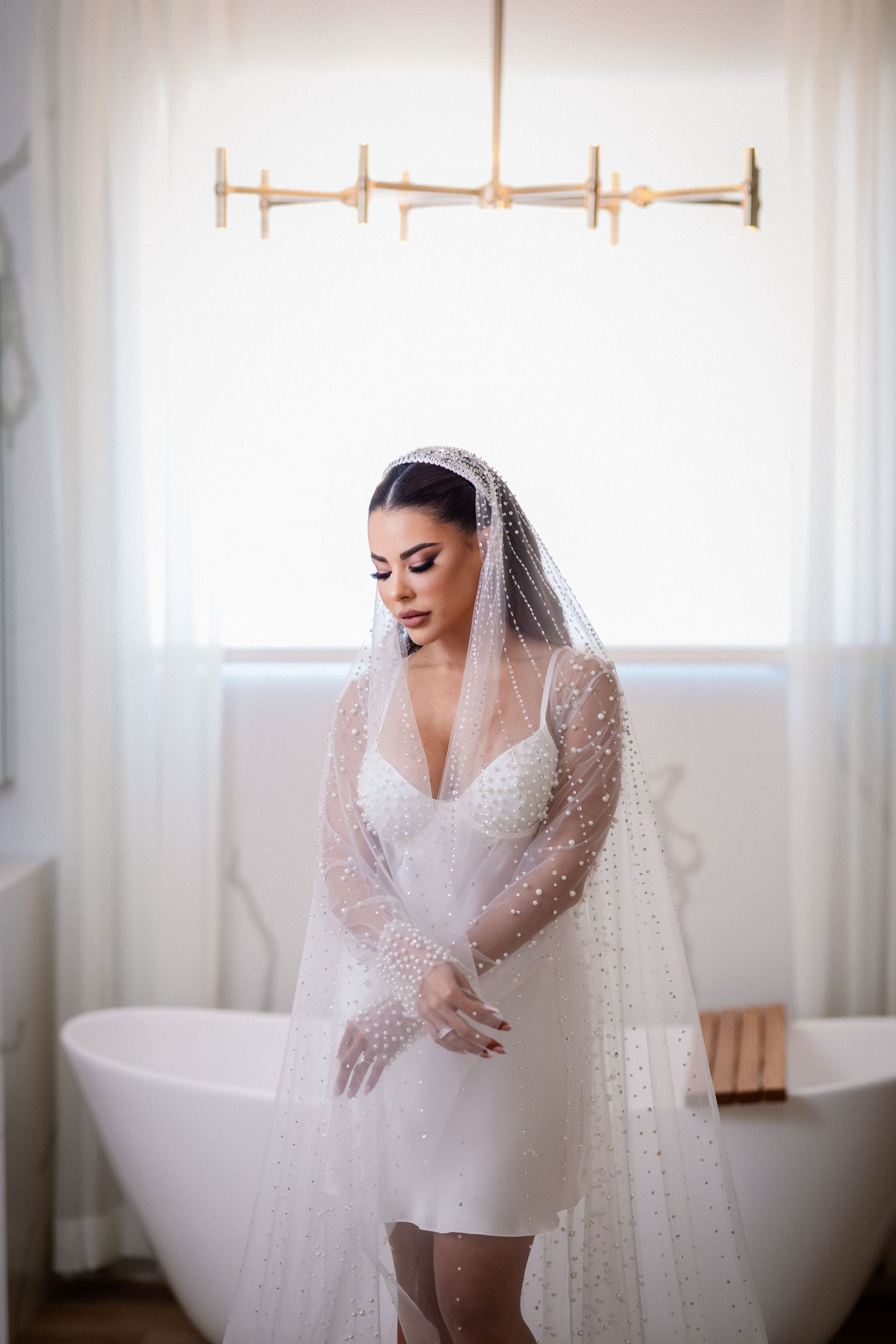 Bridal portrait in a bright white room with a modern bathtub and chandelier.
