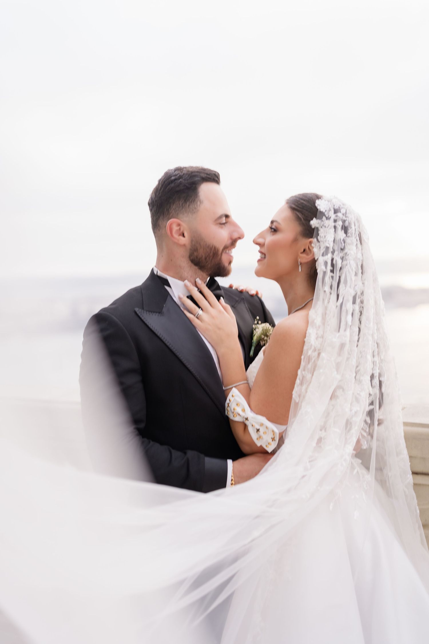 Wedding couple shares a tender moment with flowing veil against white background.