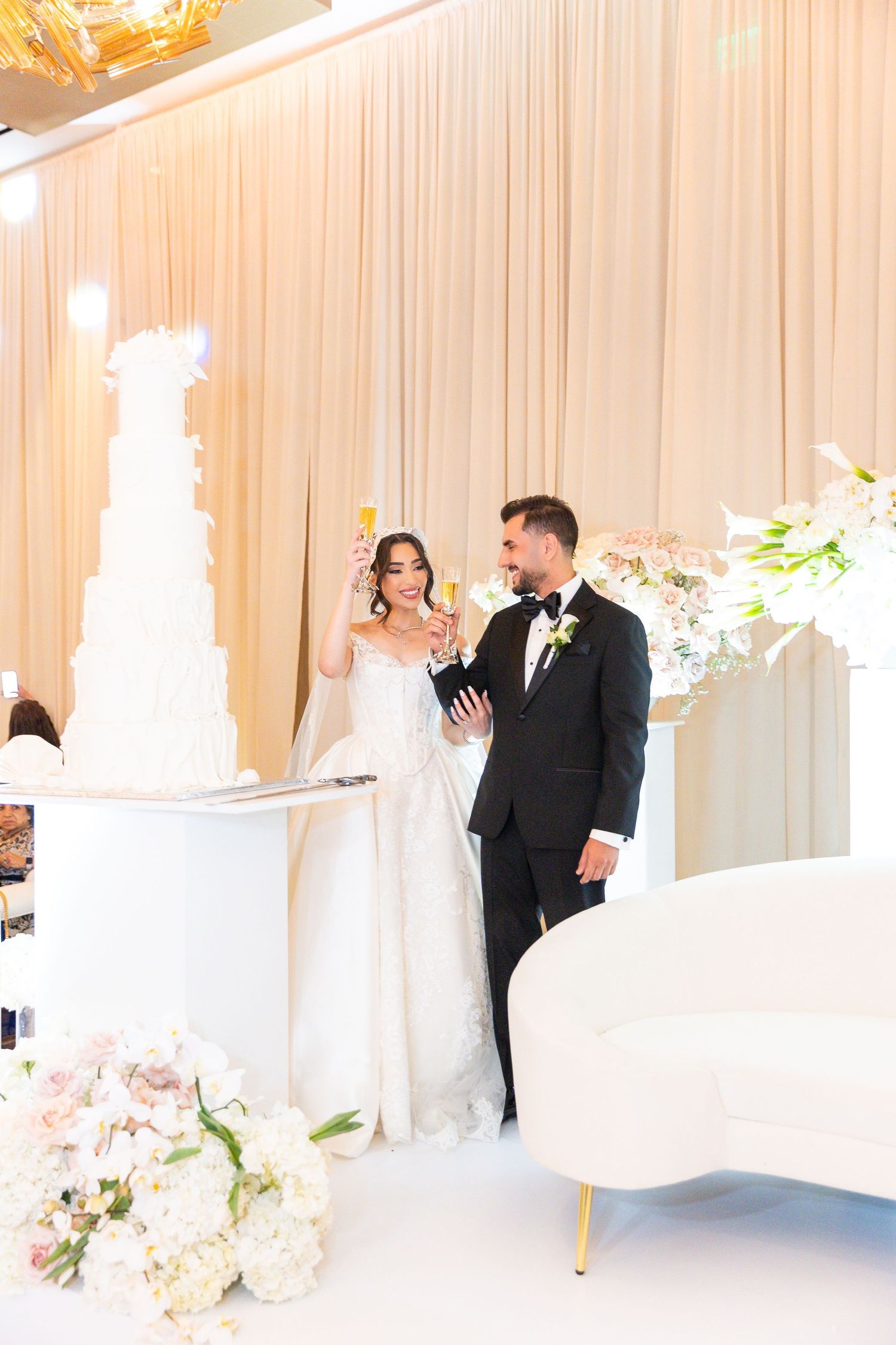 Wedding celebration in a white draped ballroom with elegant floral decorations.