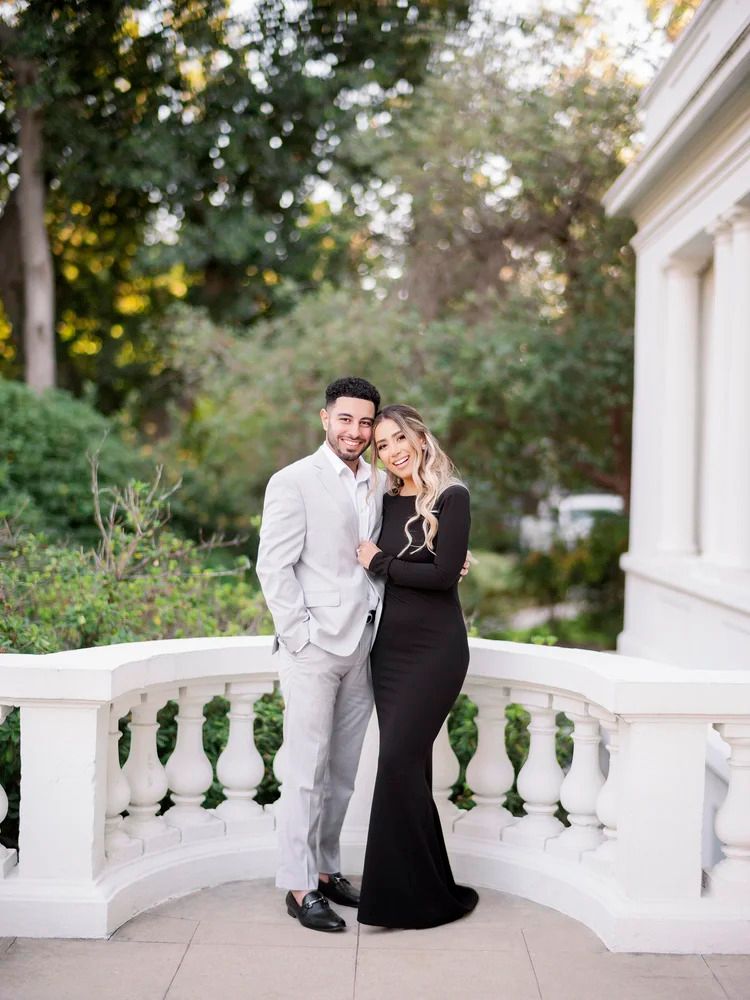 A couple shares an intimate moment on a white balcony with classical architecture and columns.