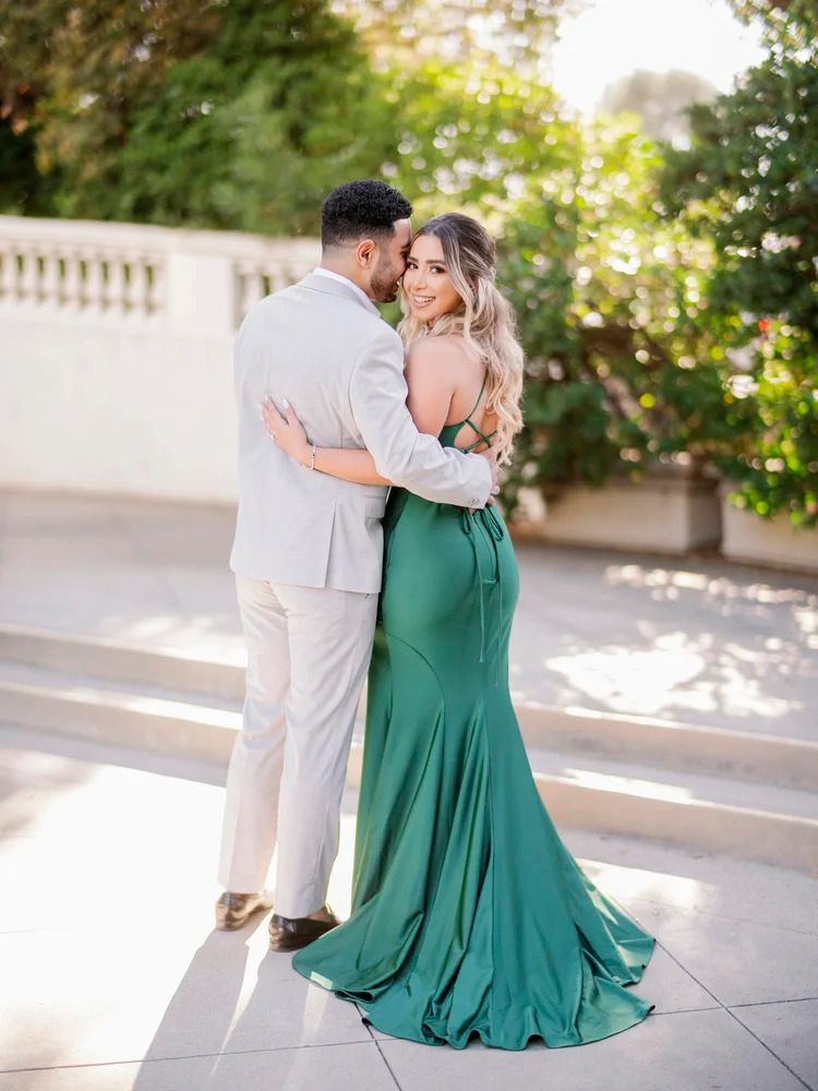 Couple in light and emerald attire dancing on sun-dappled terrace.