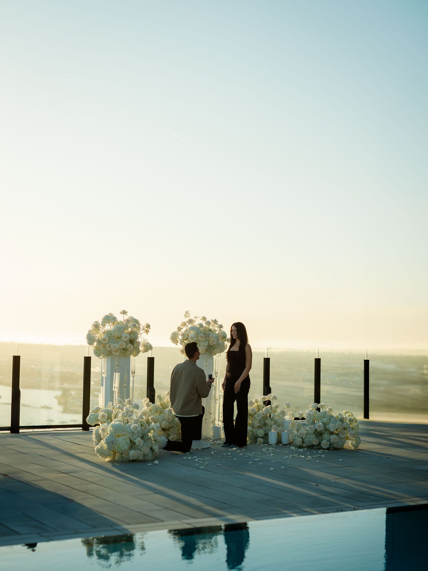 A serene rooftop proposal setup with white orchids and city views at dusk.