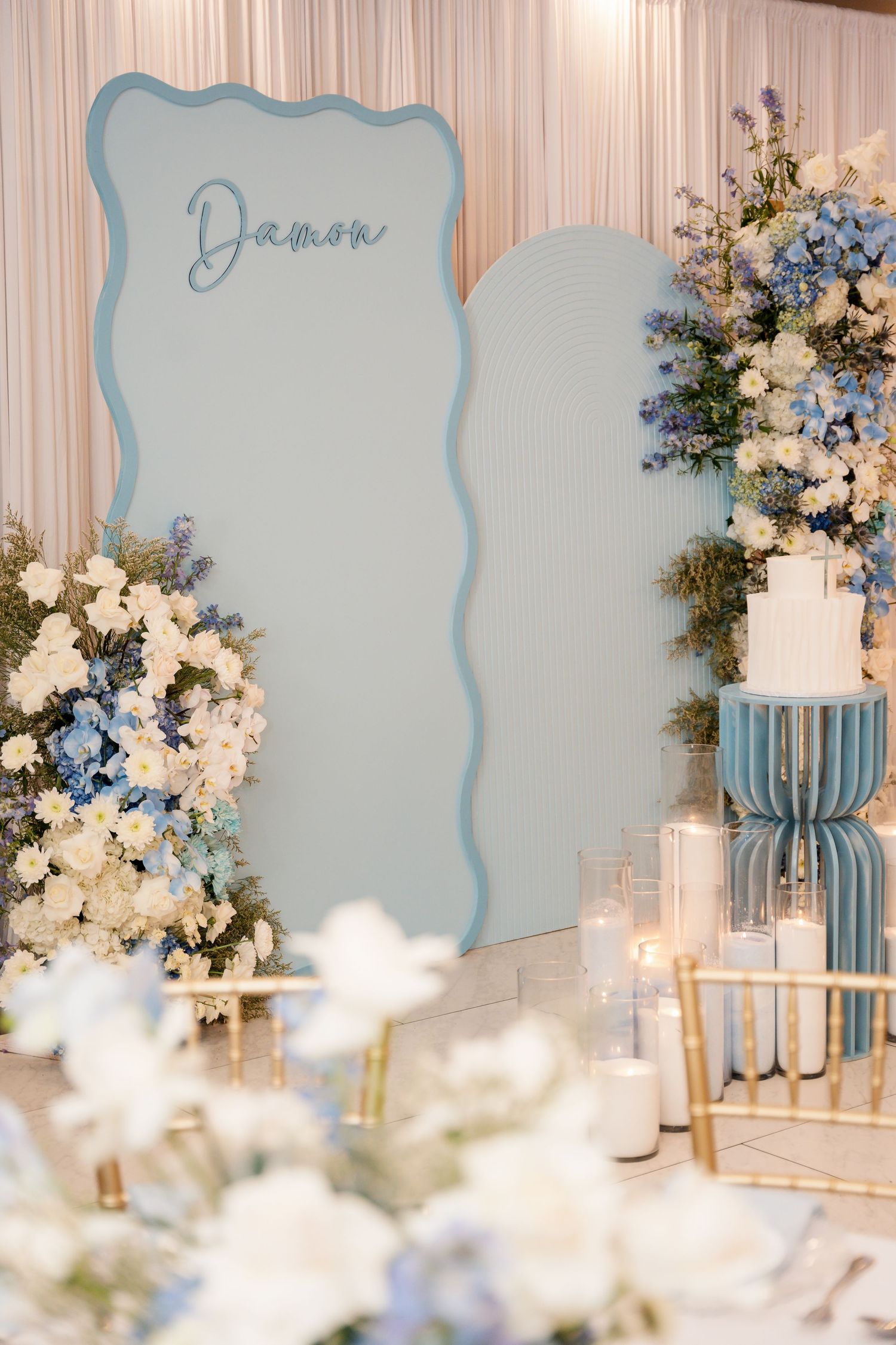 Elegant wedding reception decor featuring light blue panels and white floral arrangements with delicate lighting details.