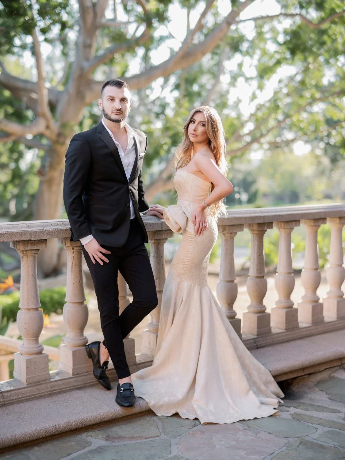 Romantic scene on stone balcony with classical balustrades and lush trees in background.