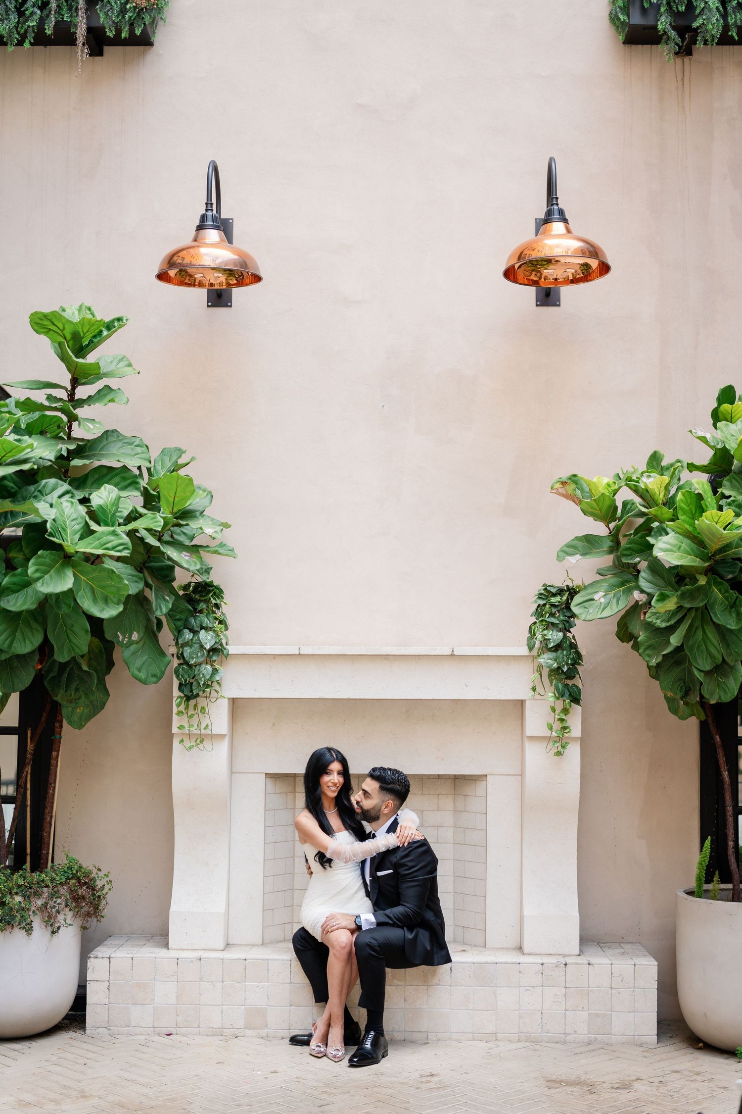 A series of romantic portraits taken in an outdoor courtyard with modern lighting and potted fiddle leaf plants.