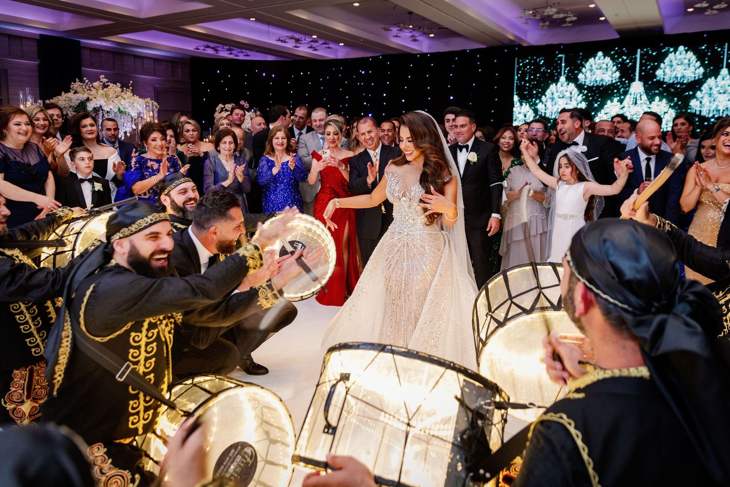 Wedding reception dance floor filled with guests celebrating under purple lighting.