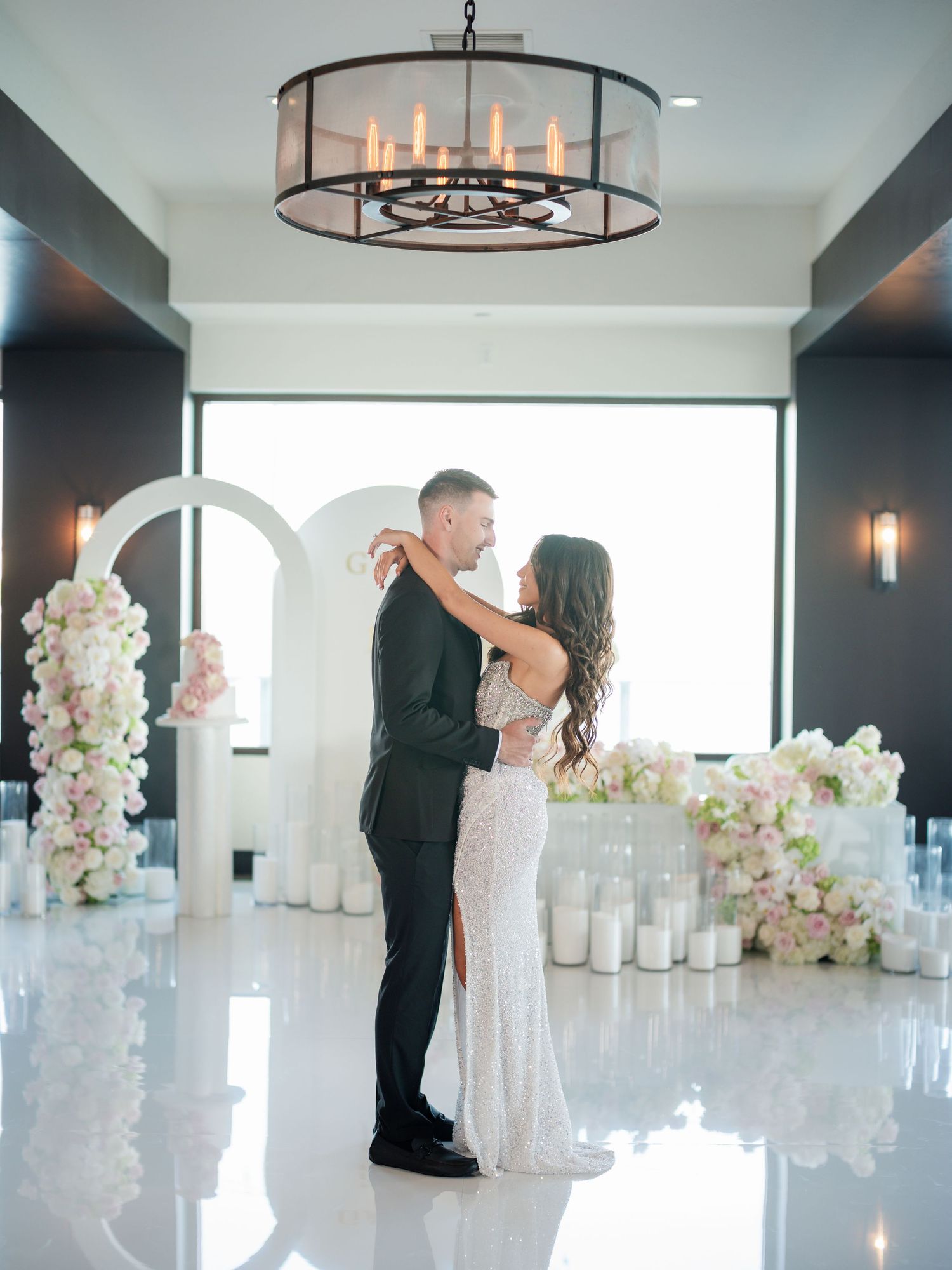 Elegant indoor celebration with crystal chandeliers, white floral arrangements and modern decor.