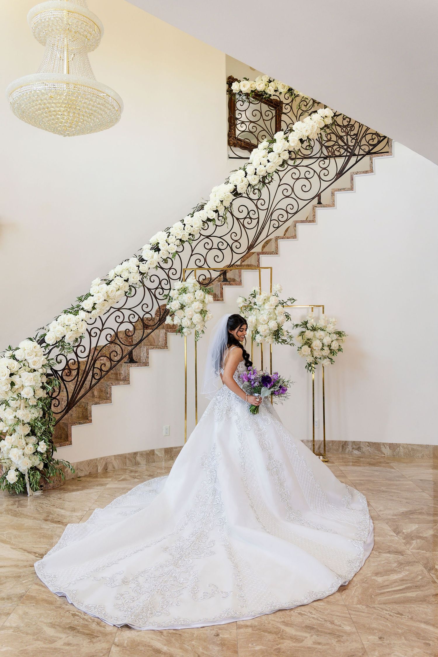 Wedding dress with long train displayed on elegant staircase decorated with white flowers.