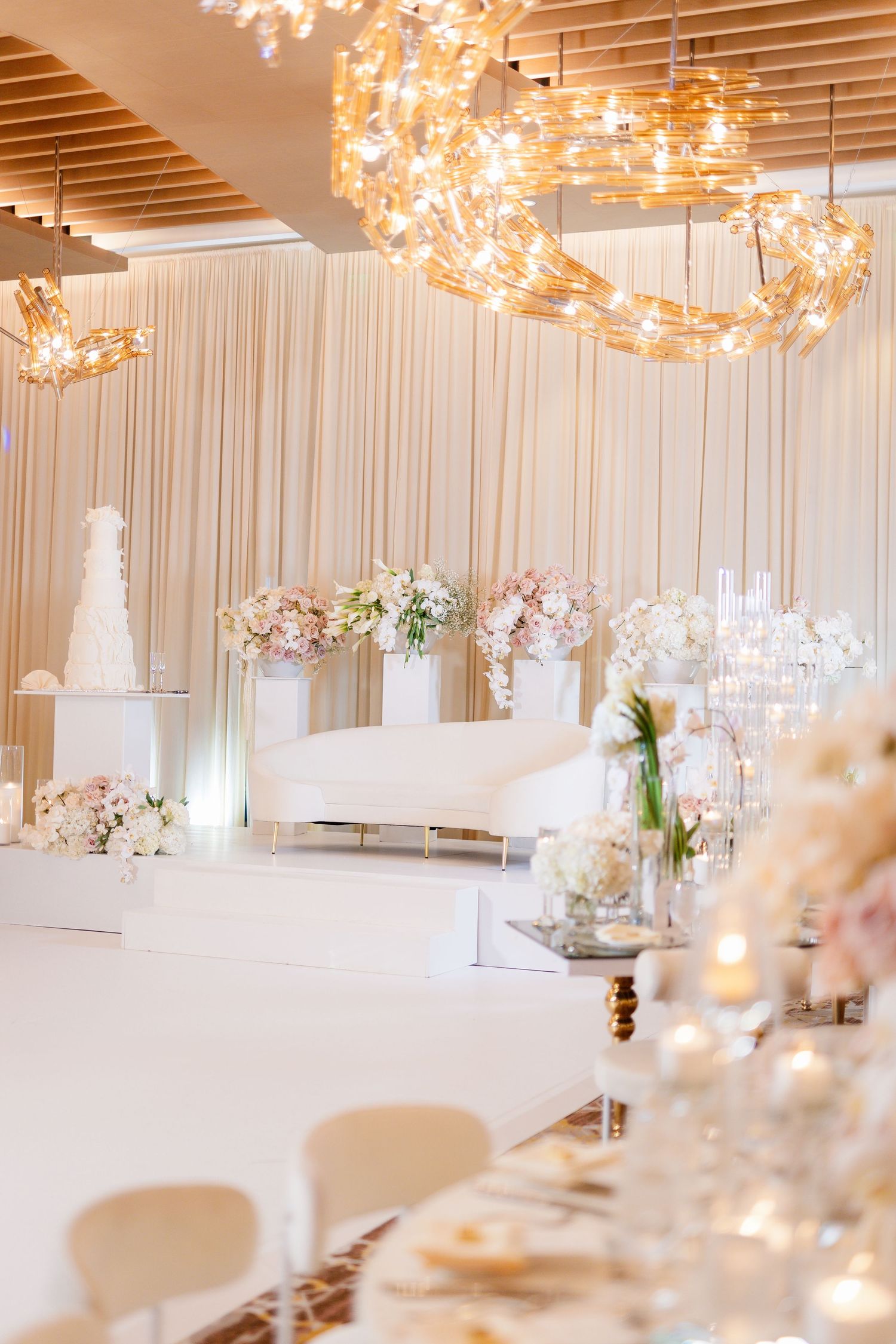 Modern white wedding reception setup with crystal chandeliers and delicate floral centerpieces.