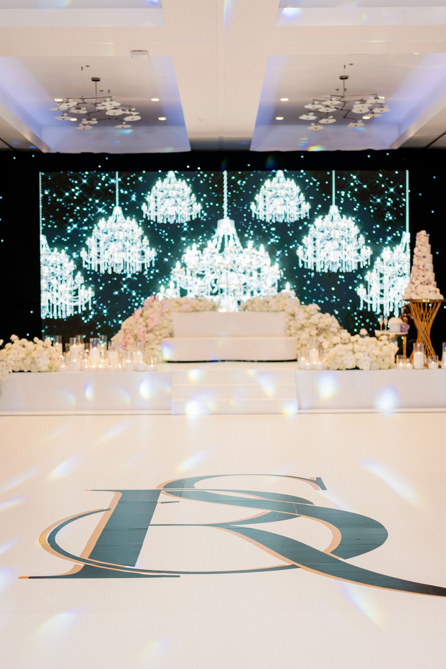 Elegant wedding reception setup with crystal chandeliers and monogram on white dance floor.