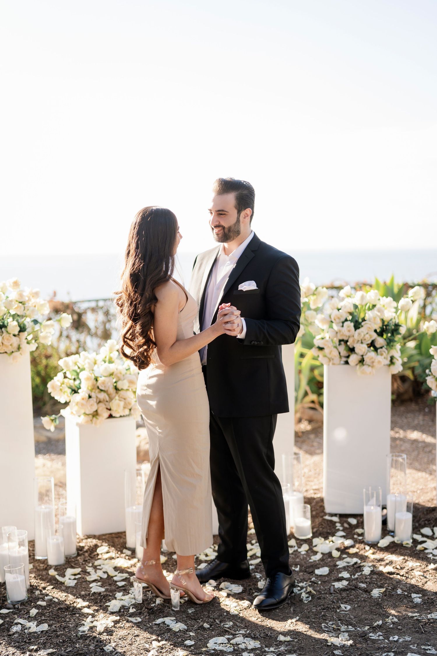 A couple shares an intimate moment among white floral pillars during a proposal.