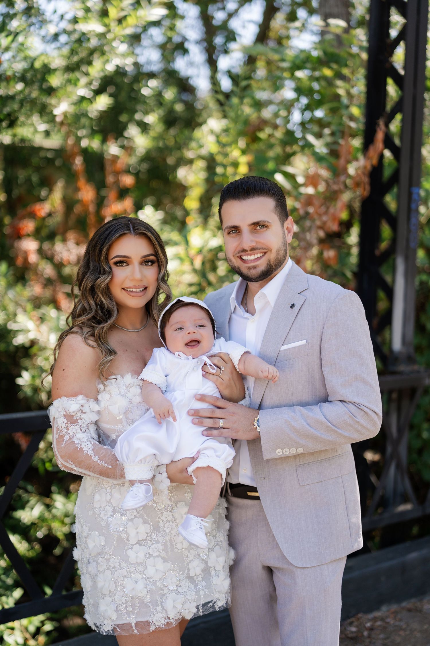 A family wearing white outfits poses together outdoors in a garden setting during a photo session.