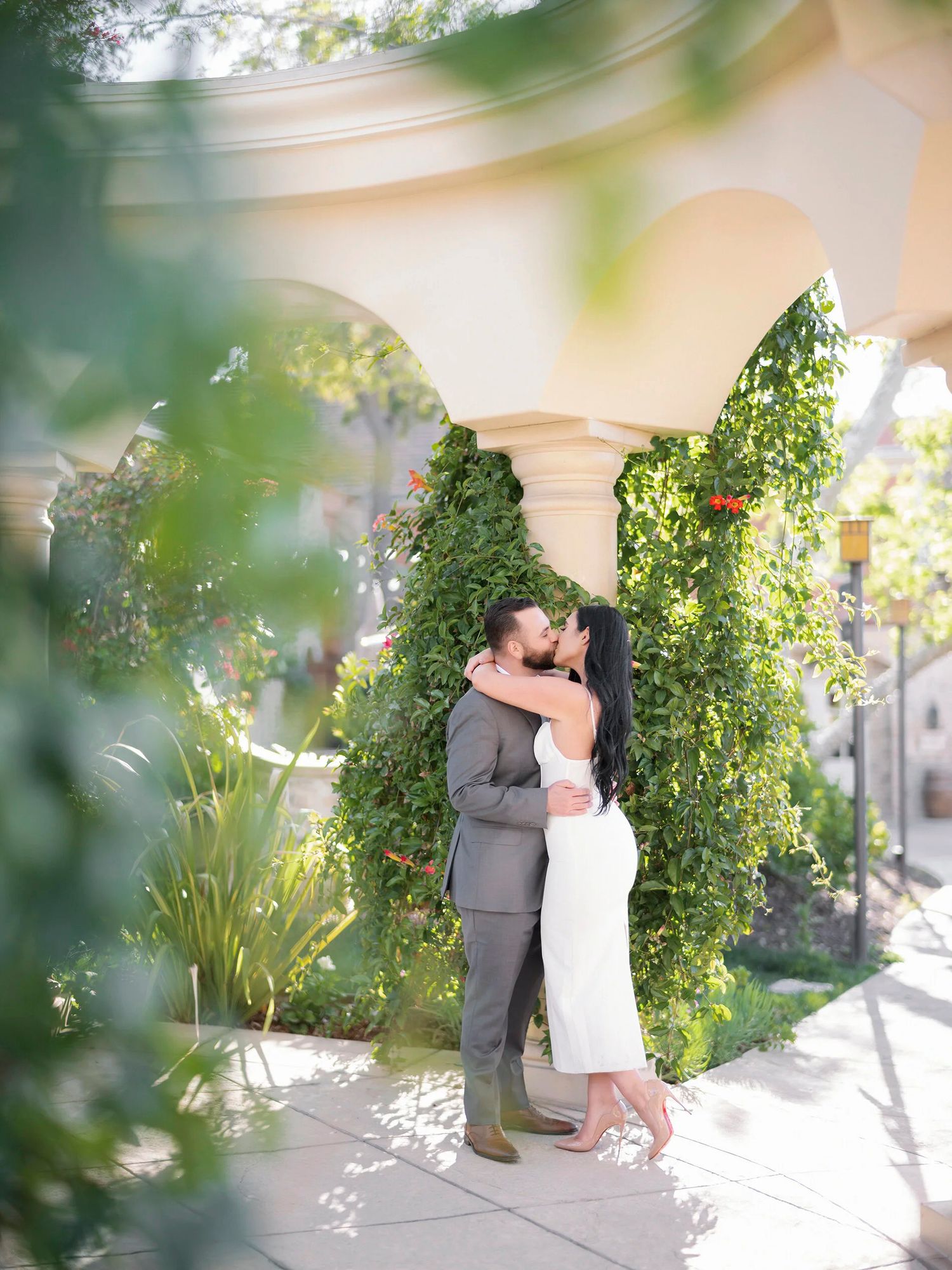 Romantic moment captured in a sunlit garden courtyard with lush greenery.