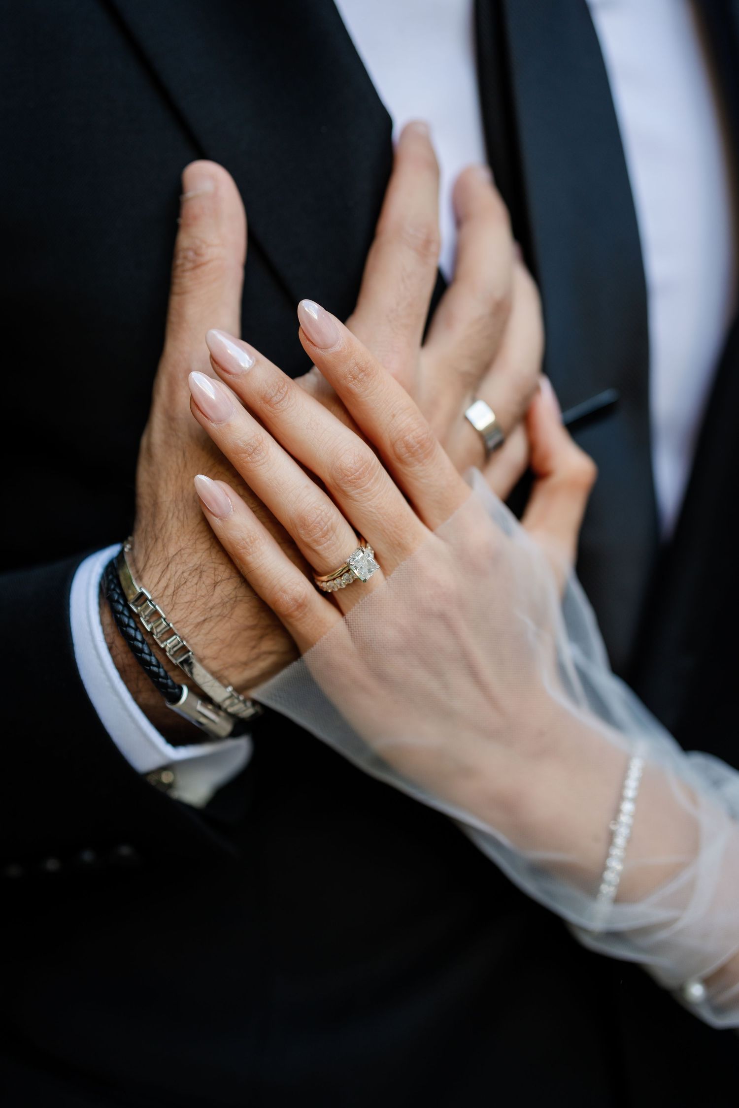 Close-up shots of hands with engagement rings and jewelry against formal black and white attire.