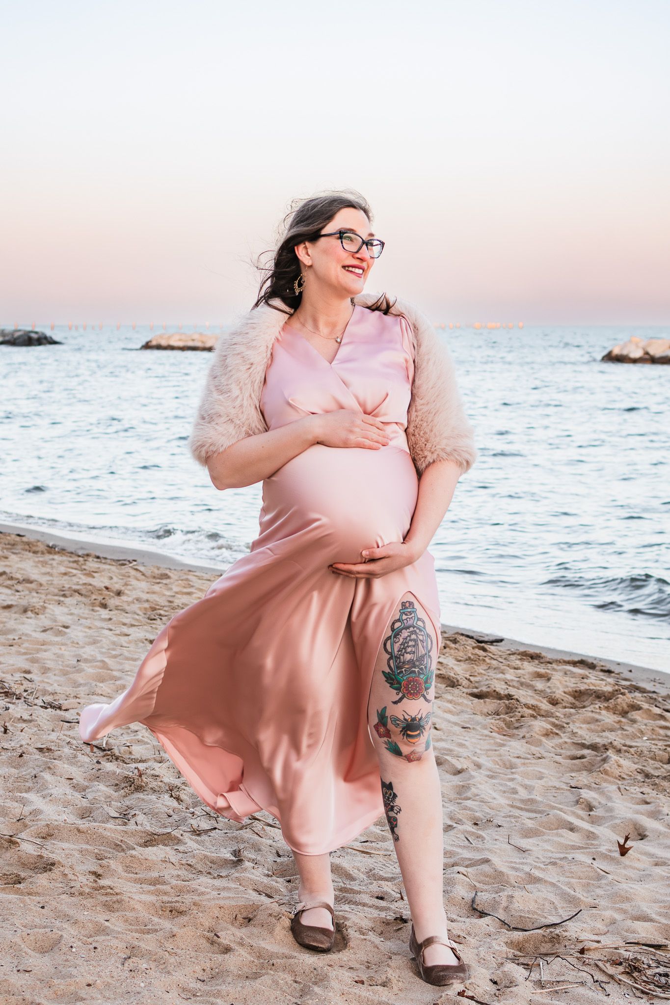 Woman standing on the beach during a maternity photo session at sunset.