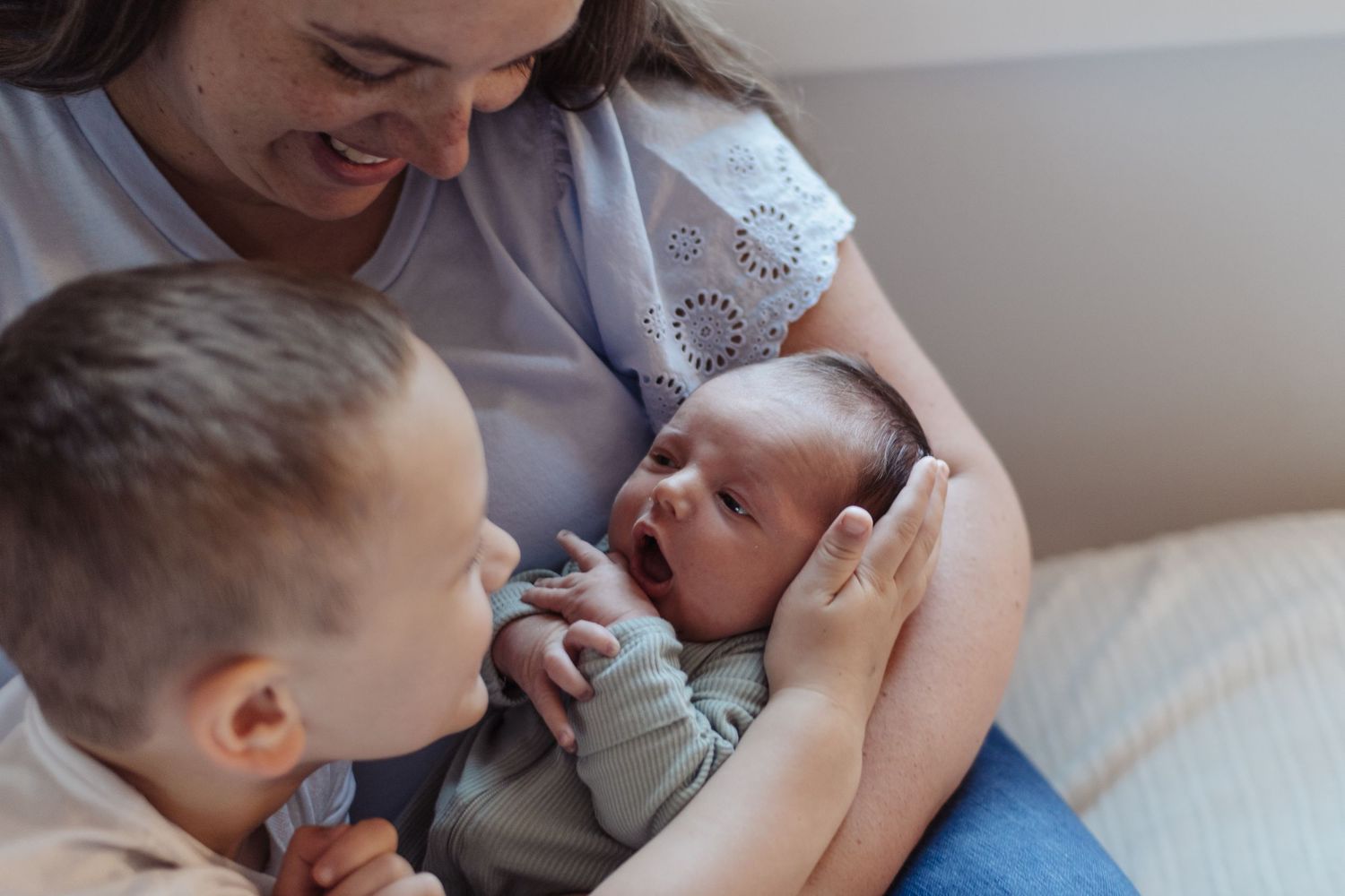 Mother and brother cradling baby during an in-home newborn lifestyle family photography session in Crofton, Maryland
