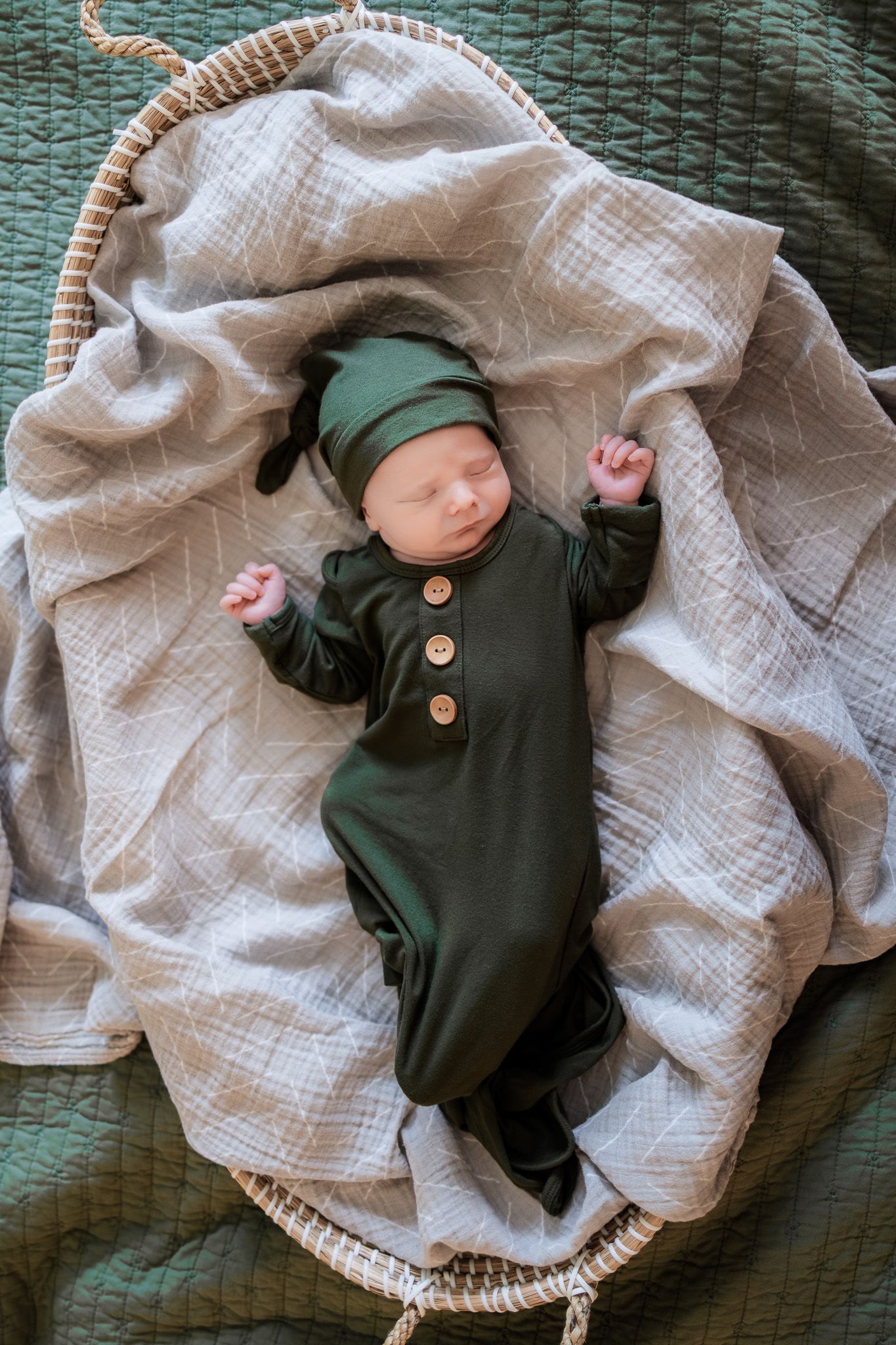 Newborn photo wearing green in a basket with blankets.