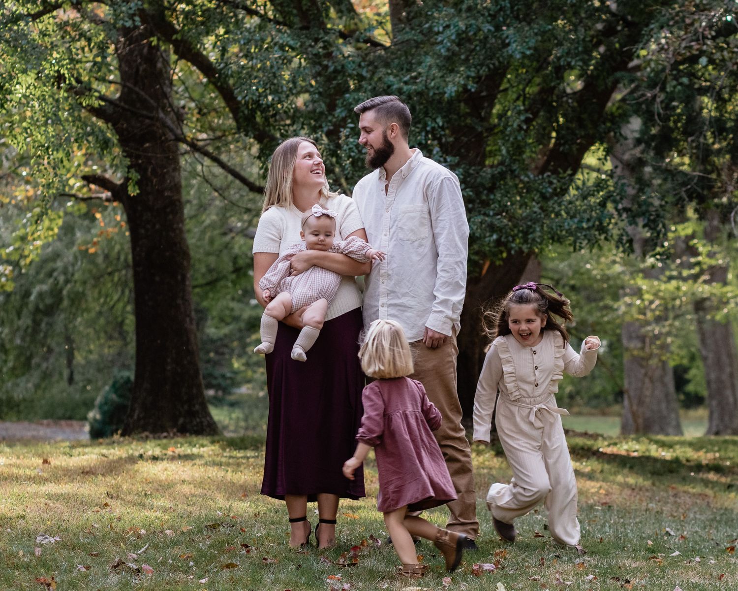 Family standing while sisters run around them during a fall mini photo session in Crofton, Maryland.