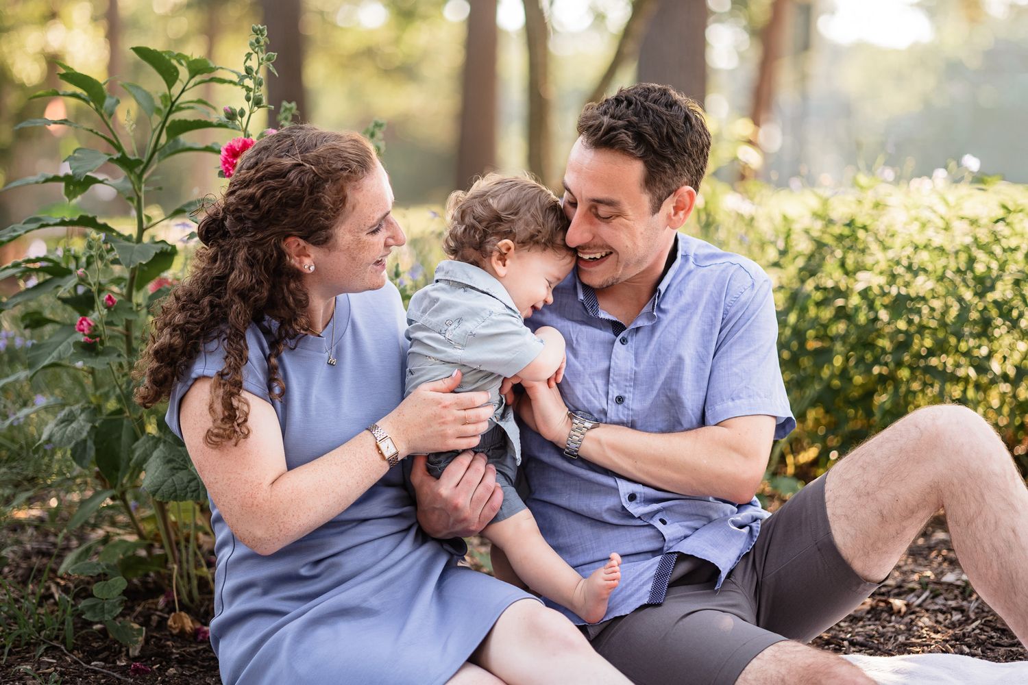 Parents holding their toddler, sitting in front of flowers at a park